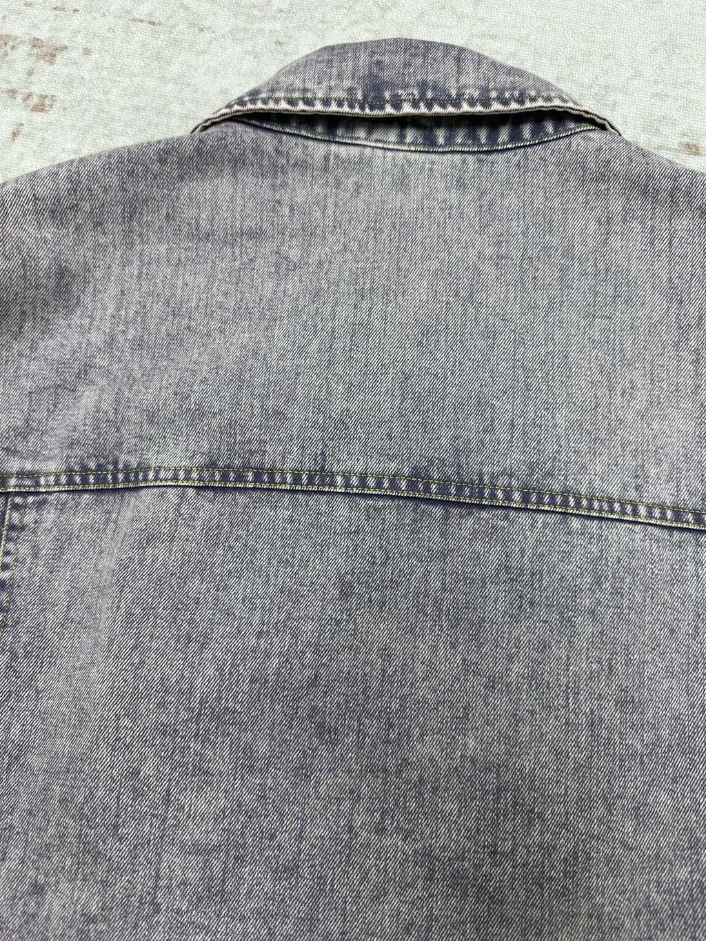 Light blue denim jacket back yoke with top-stitched seam and collar edge