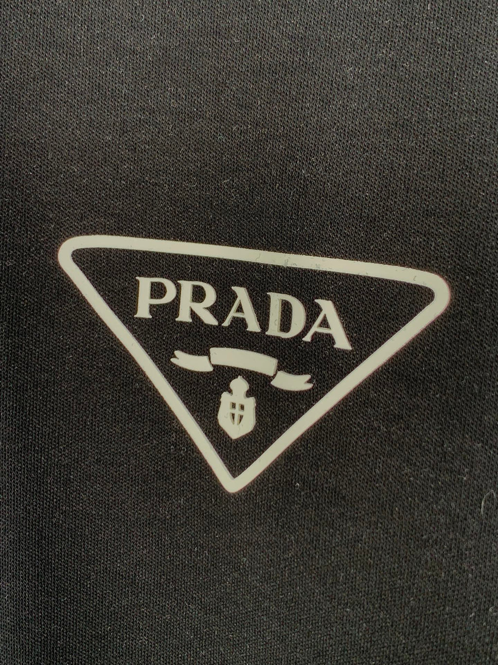 PRADA triangular logo patch on dark T-shirt fabric.