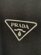 PRADA triangular logo patch on dark T-shirt fabric.