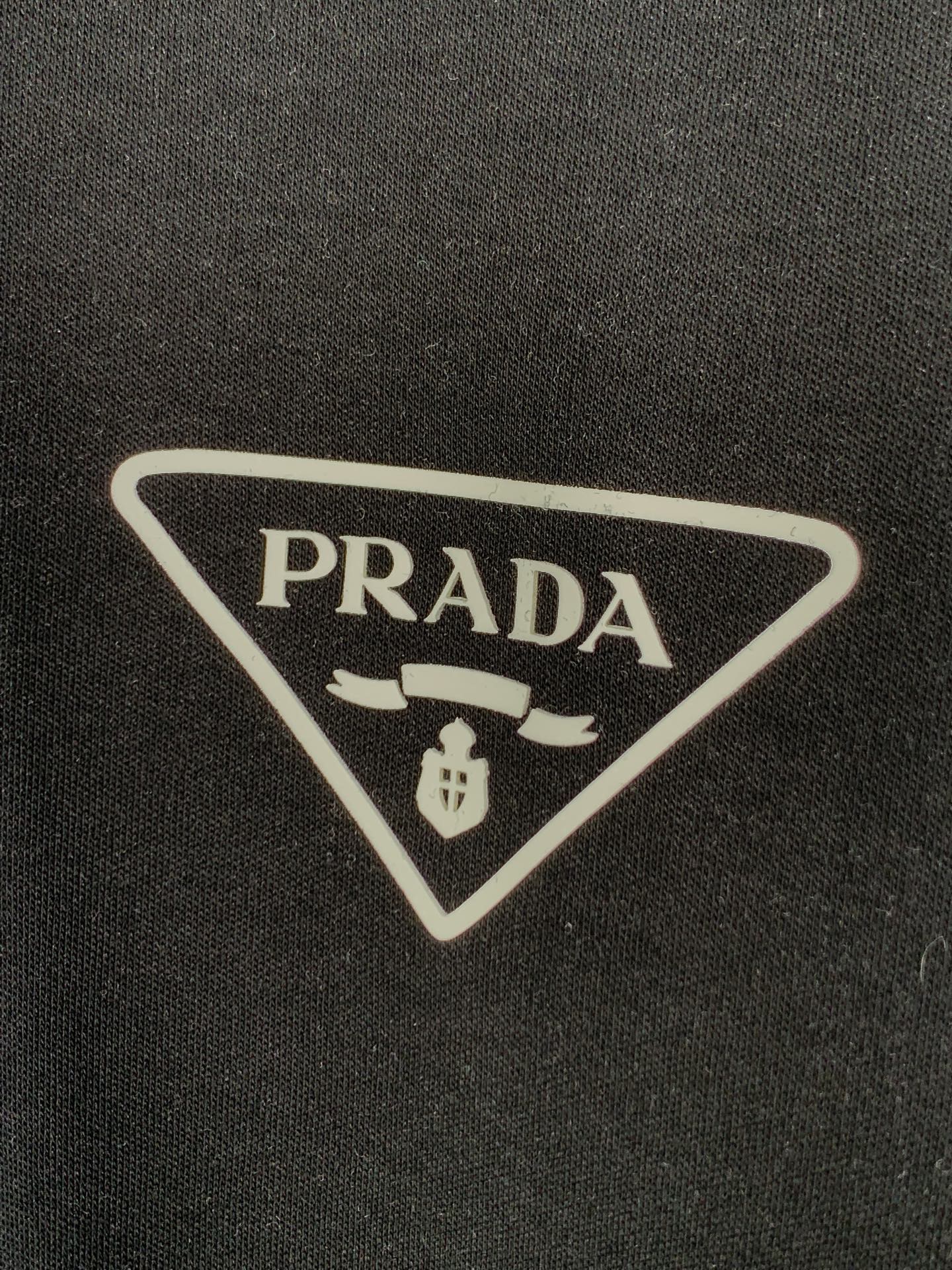 PRADA triangular logo patch on dark T-shirt fabric.