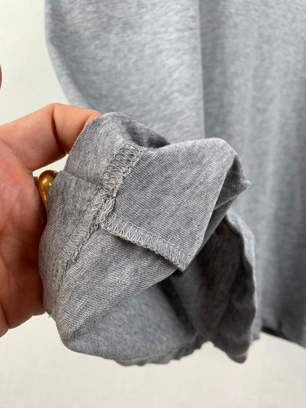 Gray T-shirt cuff and stitched hem detail, close-up held by hand.