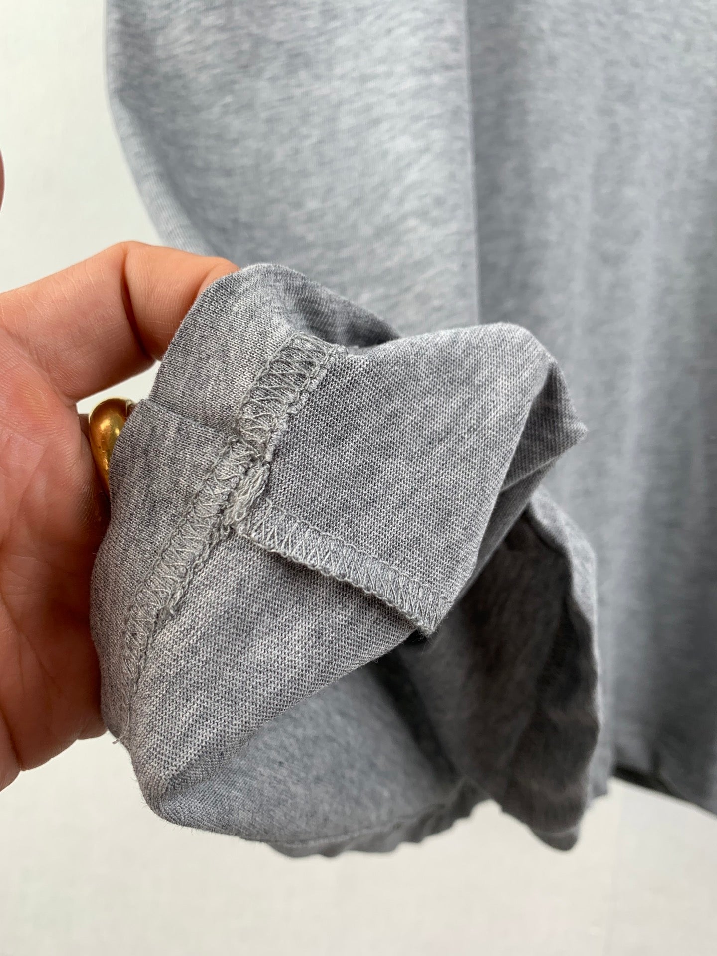 Gray T-shirt cuff and stitched hem detail, close-up held by hand.