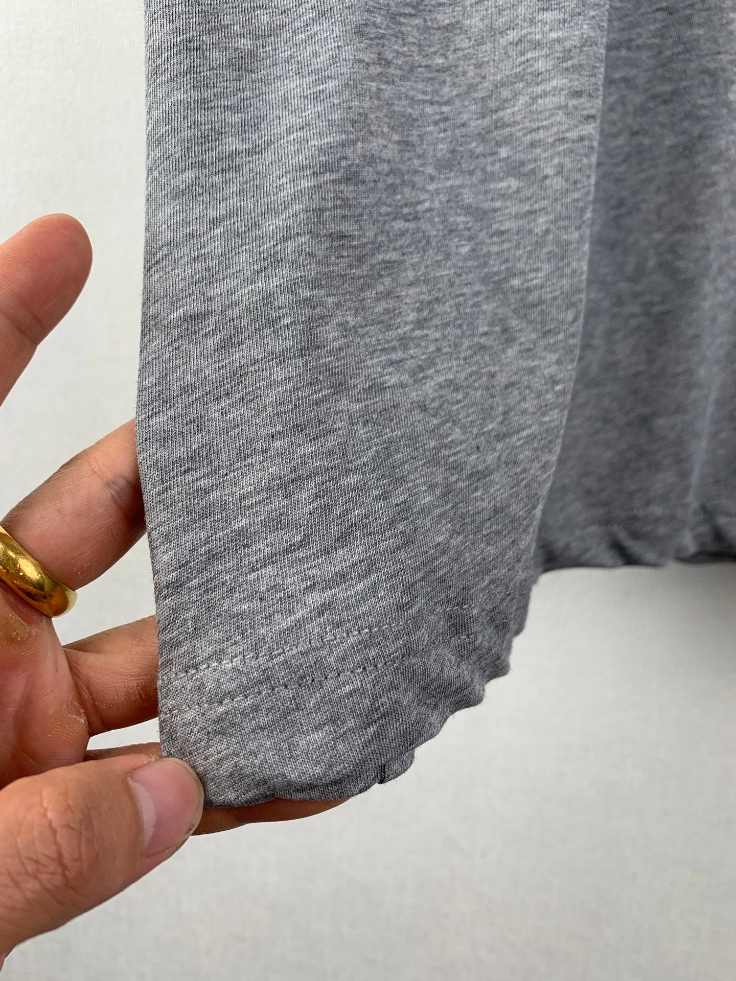 Gray T-shirt side seam and hem detail held by hand.