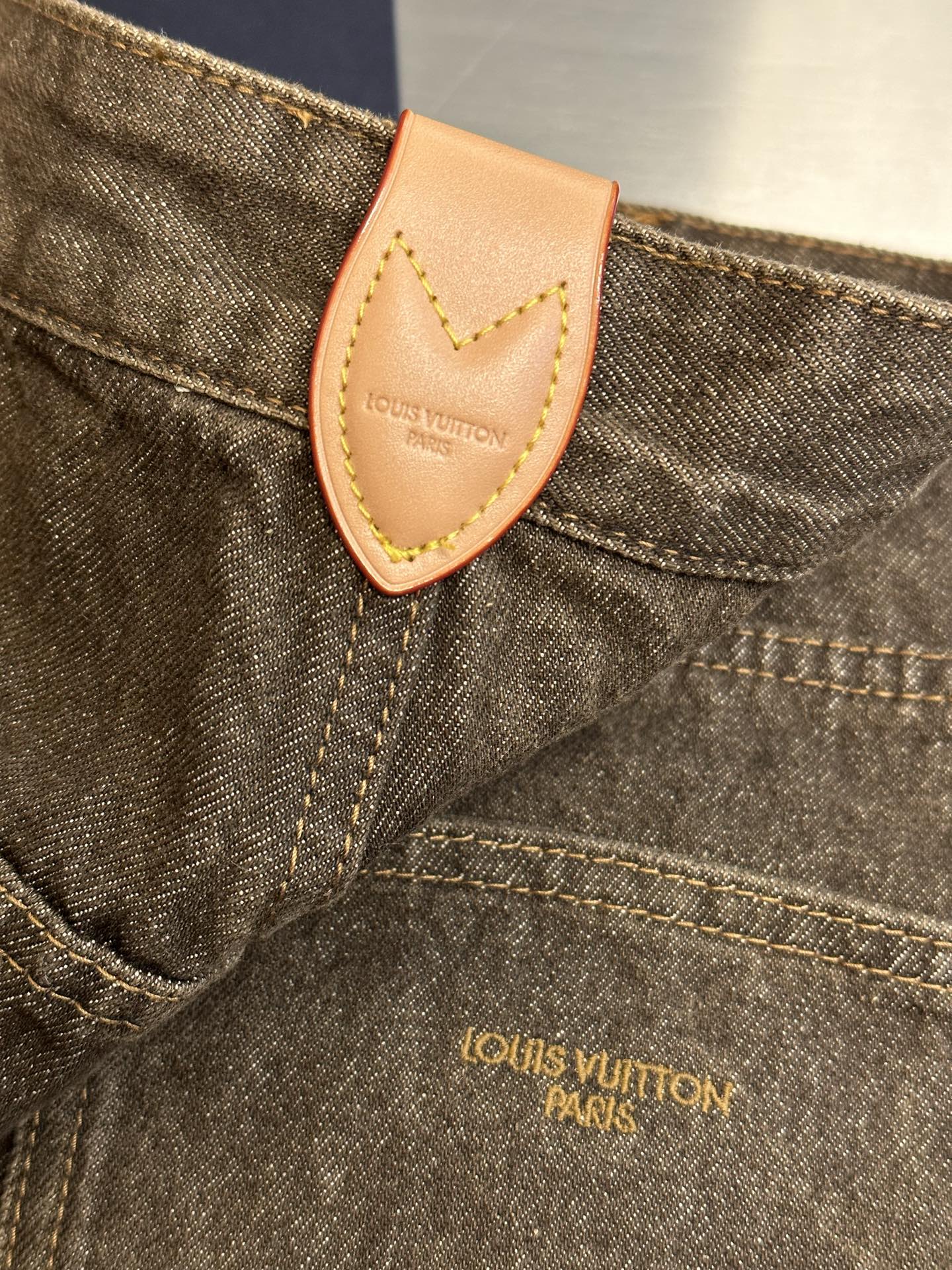 Brown denim jeans close-up, tan leather patch and Louis Vuitton Bask logo