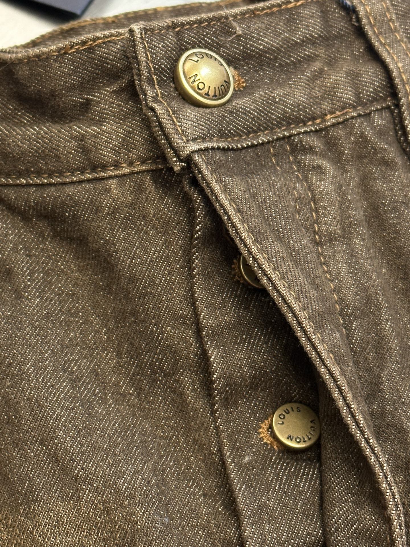 Brown denim jeans close-up, gold button detail and visible stitching