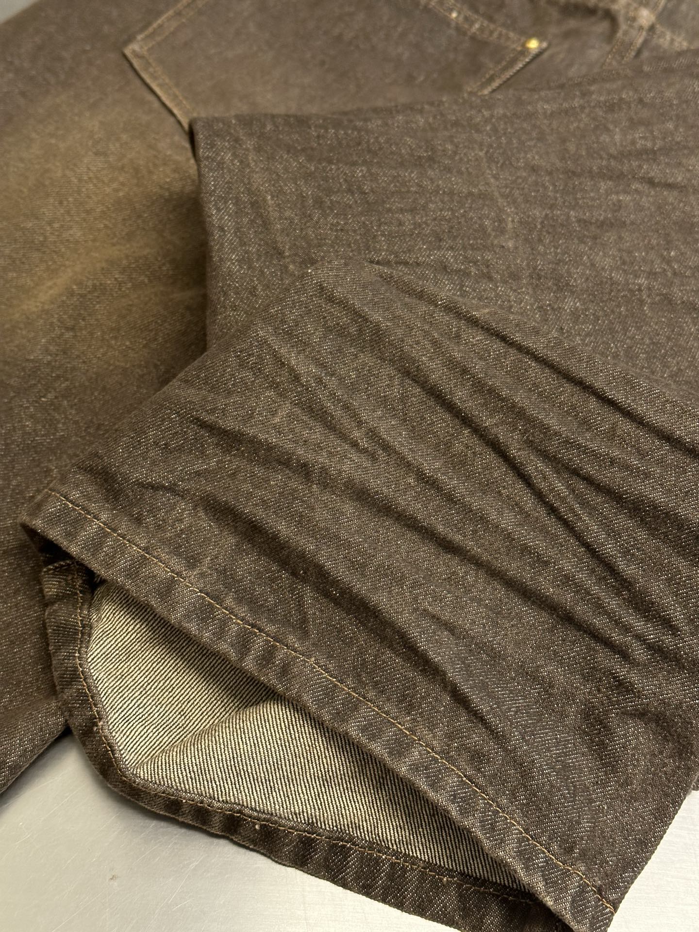 Brown denim jeans close-up, pleated fabric and stitched hem