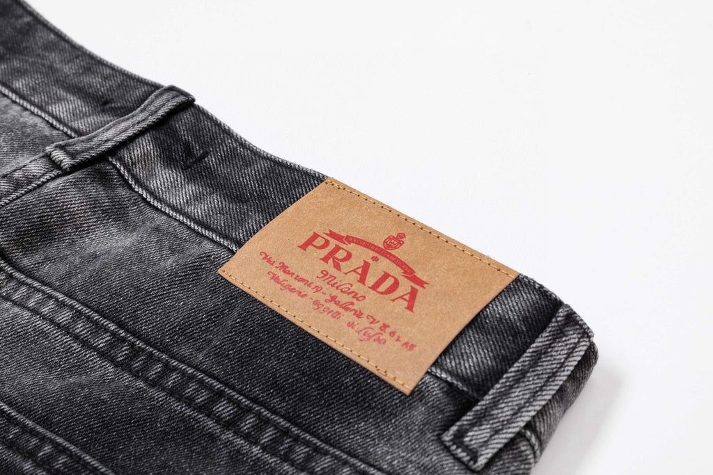 Dark gray denim pants with PRADA orange brand patch on waistband