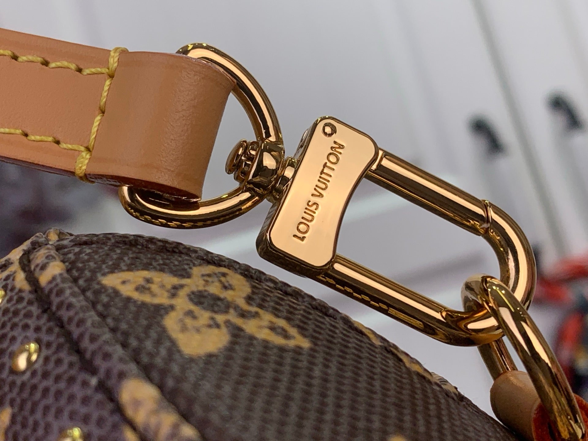 Louis Vuitton gold keychain clasp on monogram bag with tan leather strap, close-up