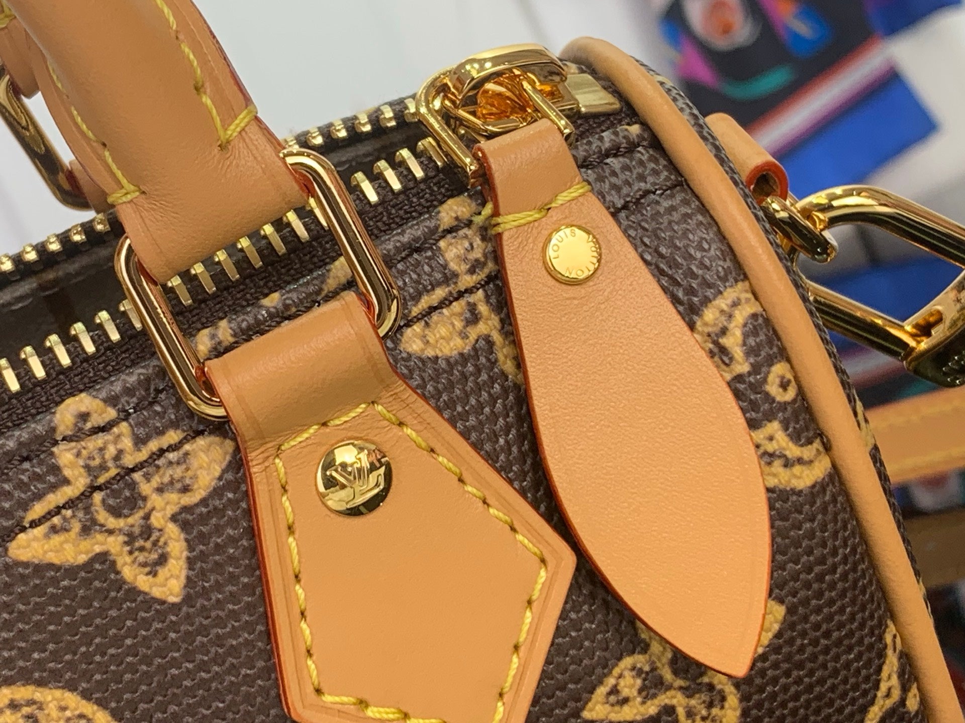 Tan leather strap and corner hardware on brown monogram bag, with gold-tone fittings.
