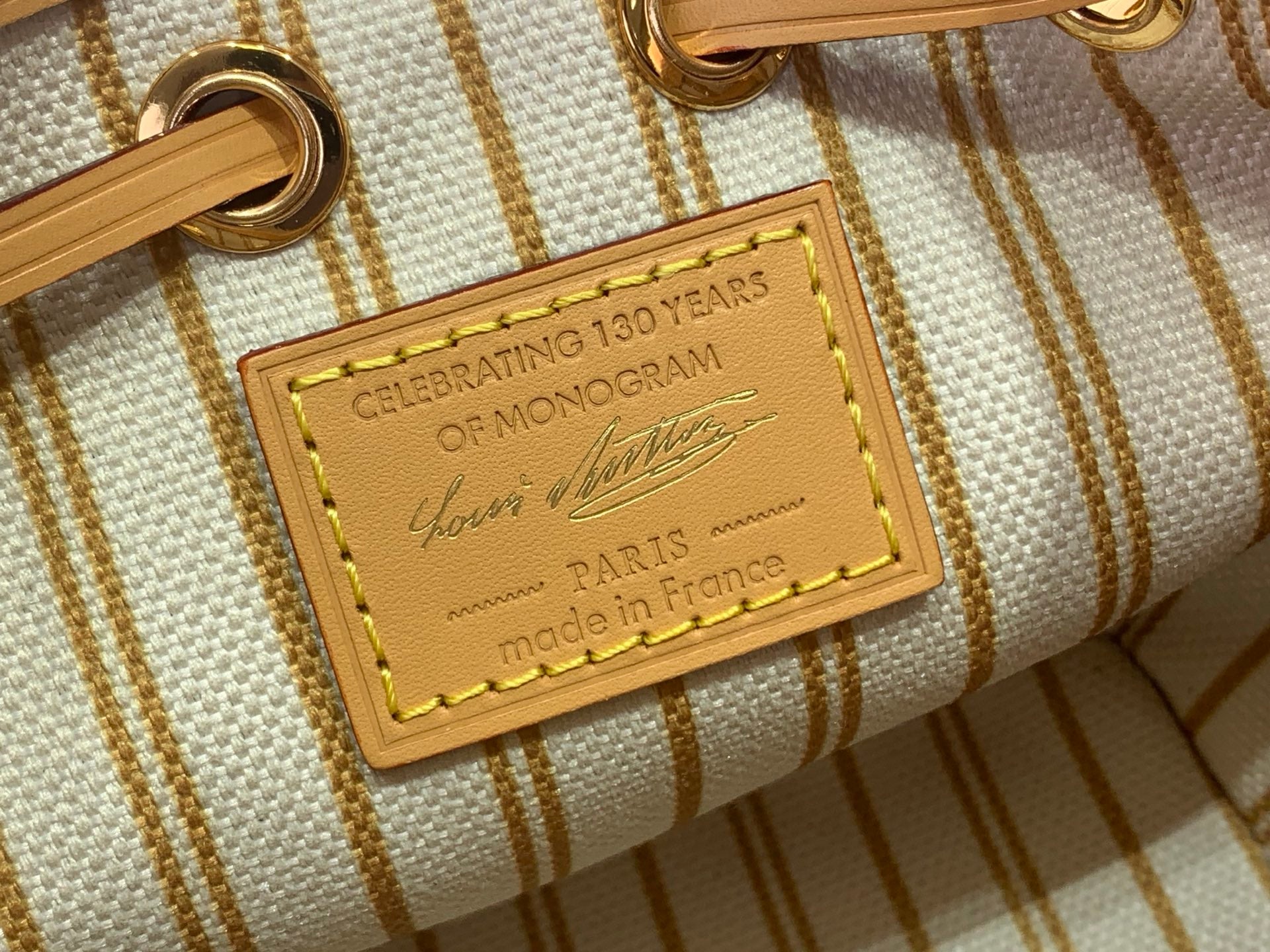 White monogram bag fabric tag with gold text celebrating 130 years