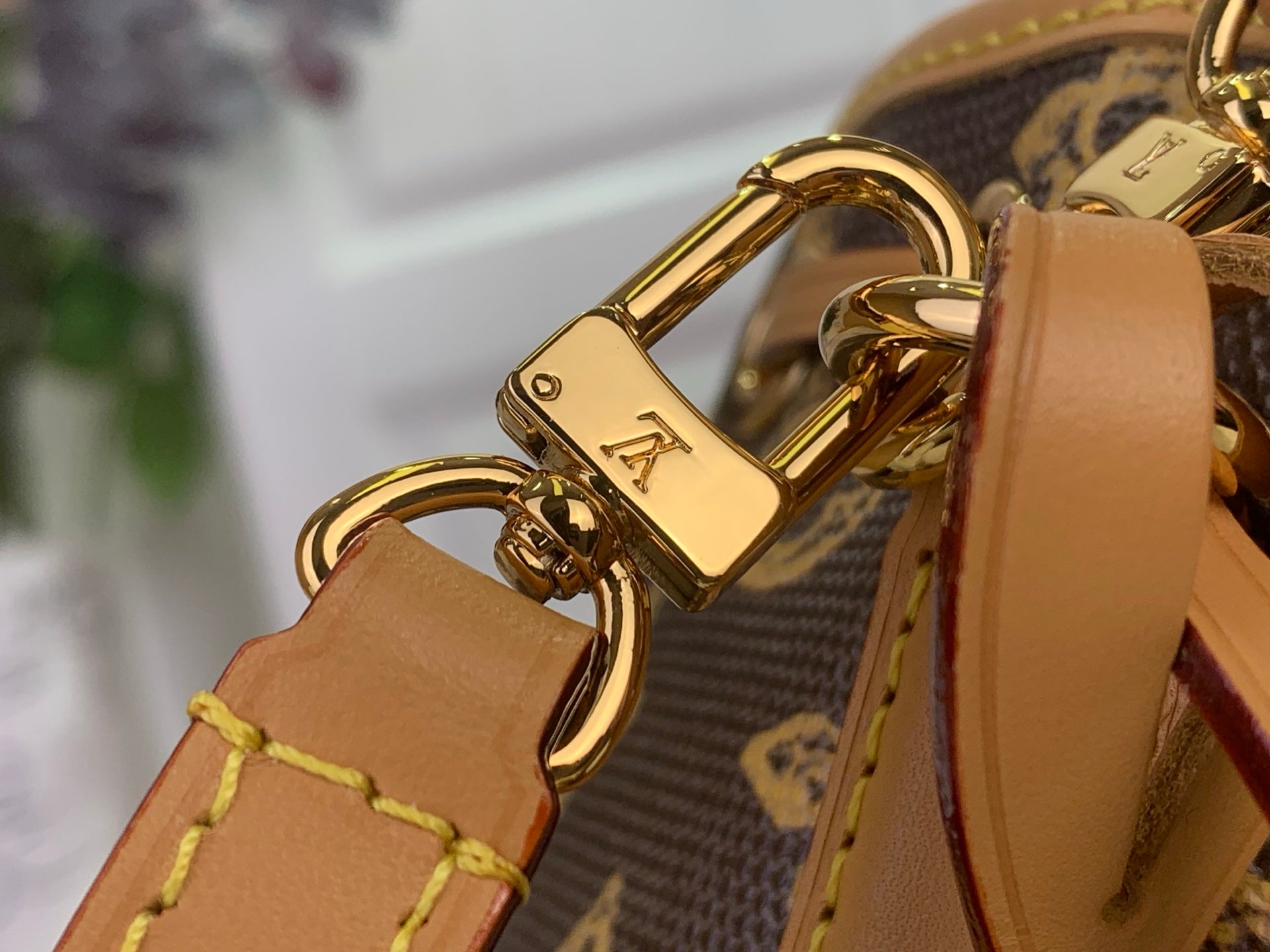 Gold-tone clasp hardware with tan leather tabs on a monogram bag strap