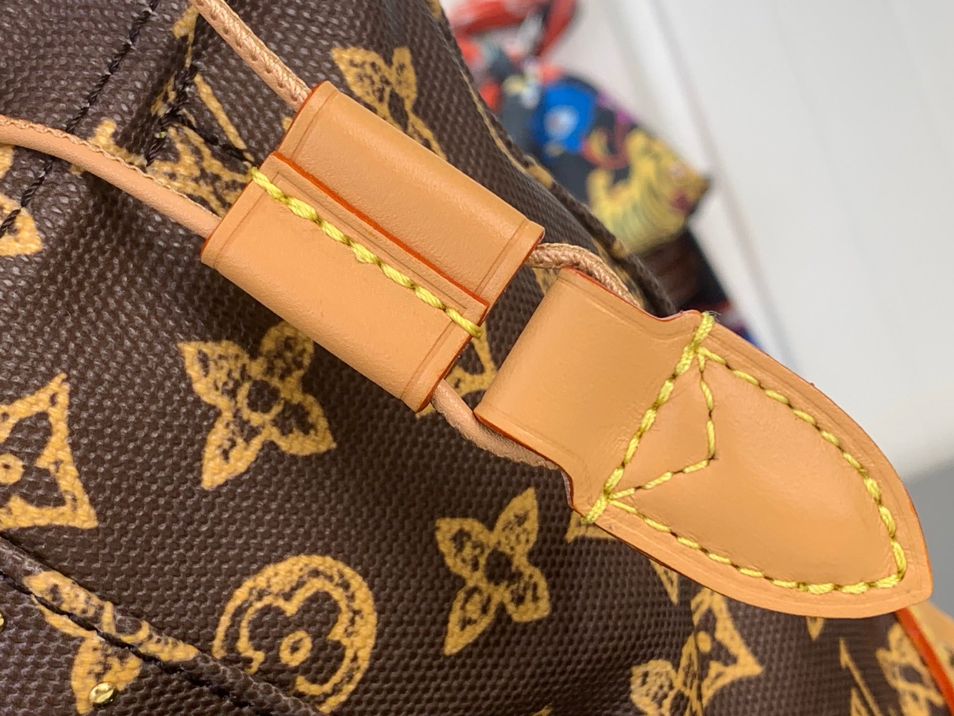 Tan leather strap end with snap closure and stitched detail on monogram canvas
