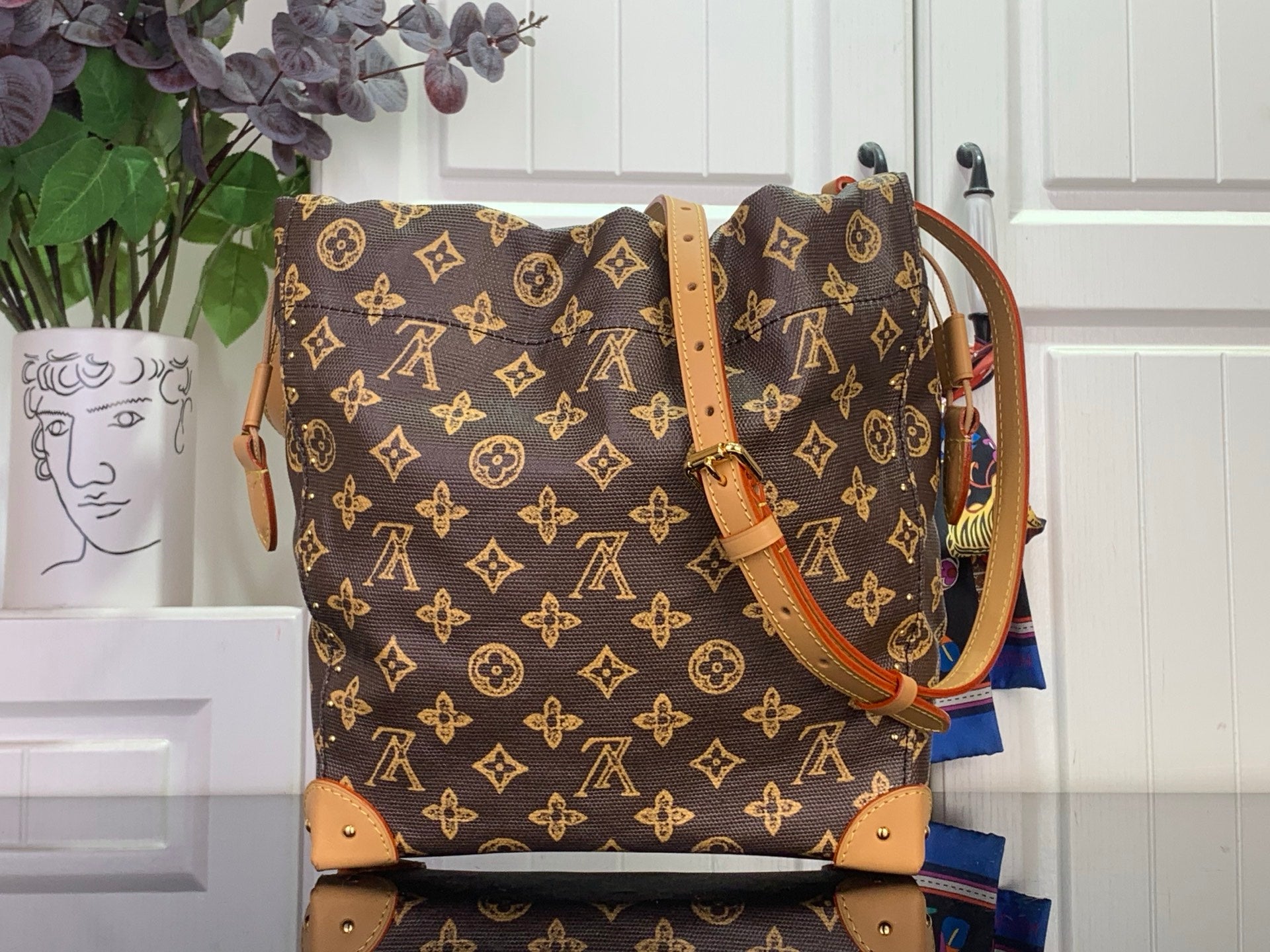 Monogram canvas bucket bag with tan leather handles and gold chain strap hardware