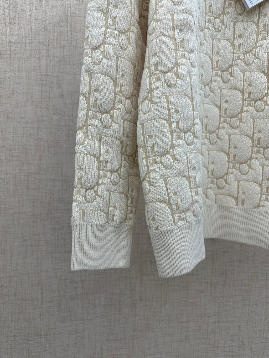 Cream knit sweater showing hem and ribbed cuffs, allover logo pattern