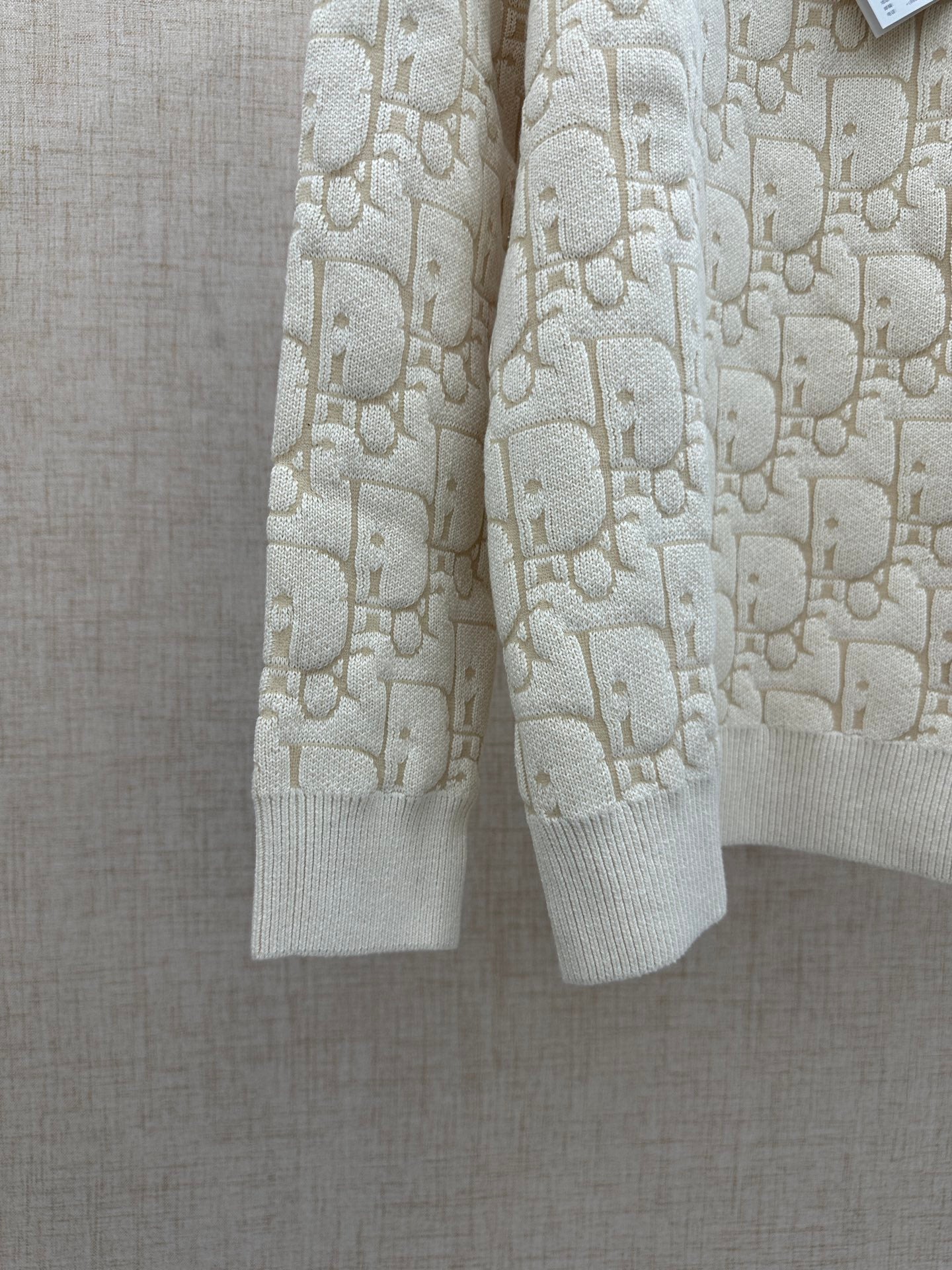 Cream knit sweater showing hem and ribbed cuffs, allover logo pattern