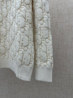 Cream knit sweater side view with allover logo pattern and ribbed hem