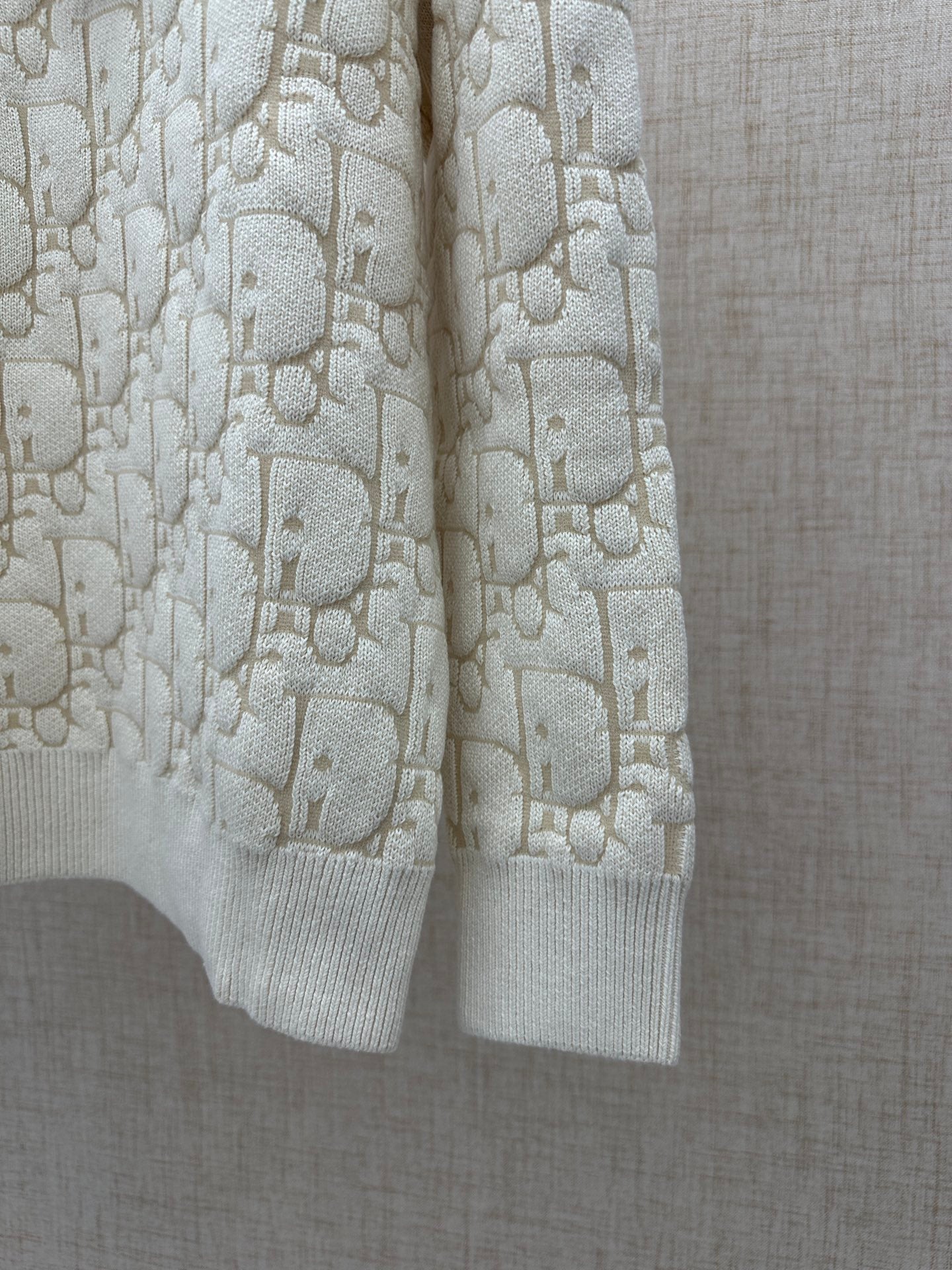 Cream knit sweater side view with allover logo pattern and ribbed hem