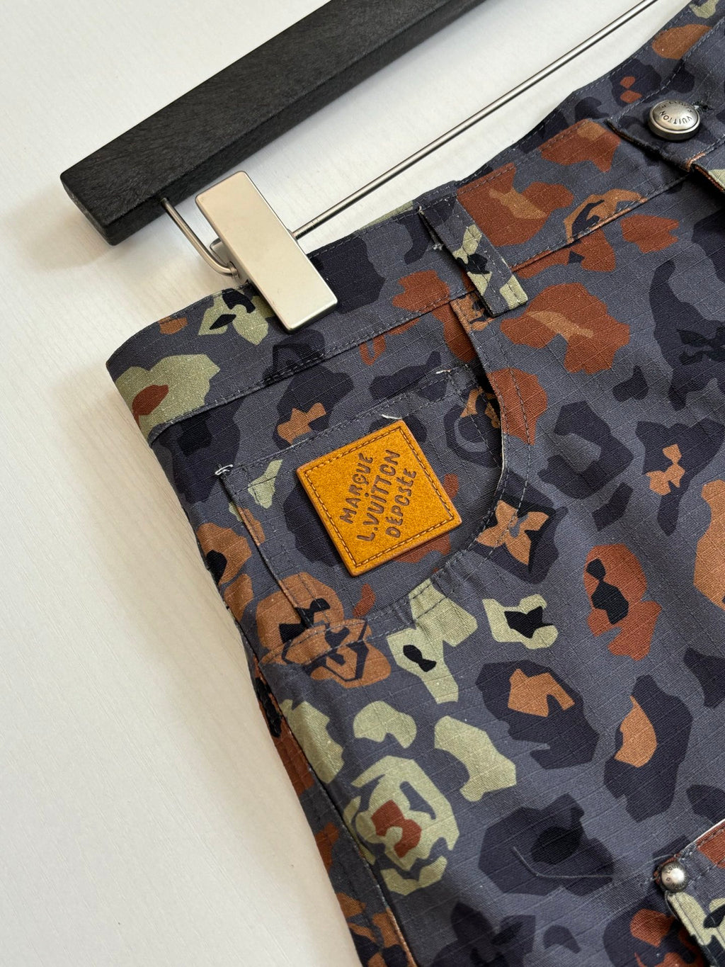 Louis Vuitton patterned shorts fabric close-up, tan patch logo on camo print