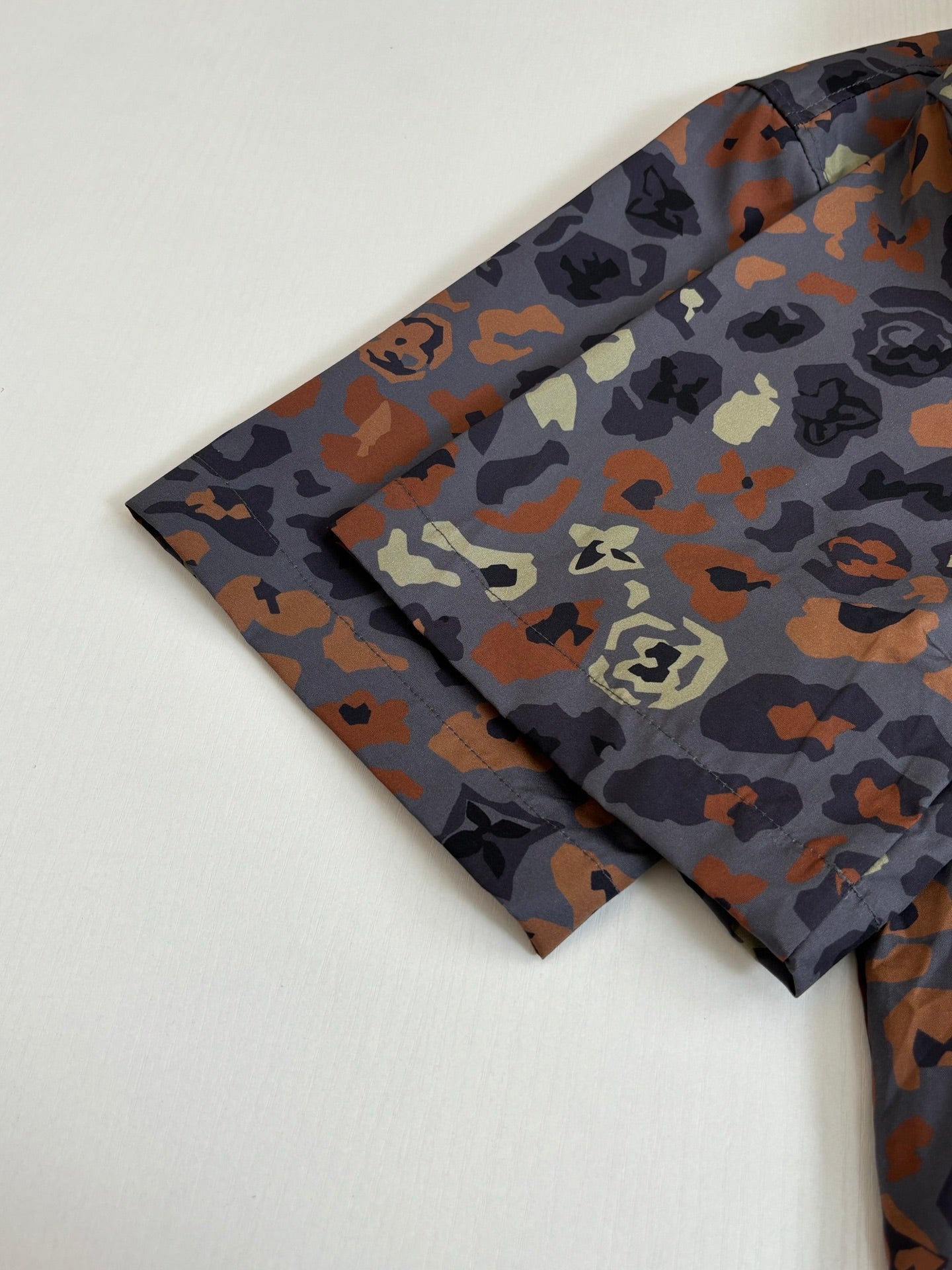 Multicolor camo shirt sleeve and shoulder laid flat on light fabric