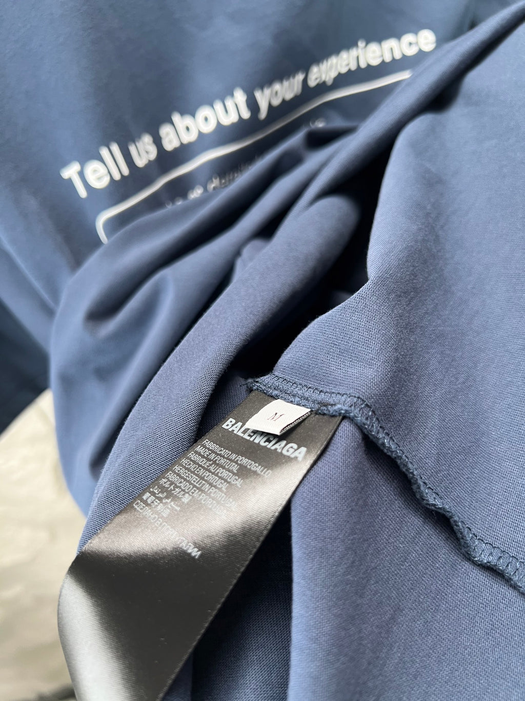 Blue T-shirt collar label and 'Tell us about your experience' text on fabric
