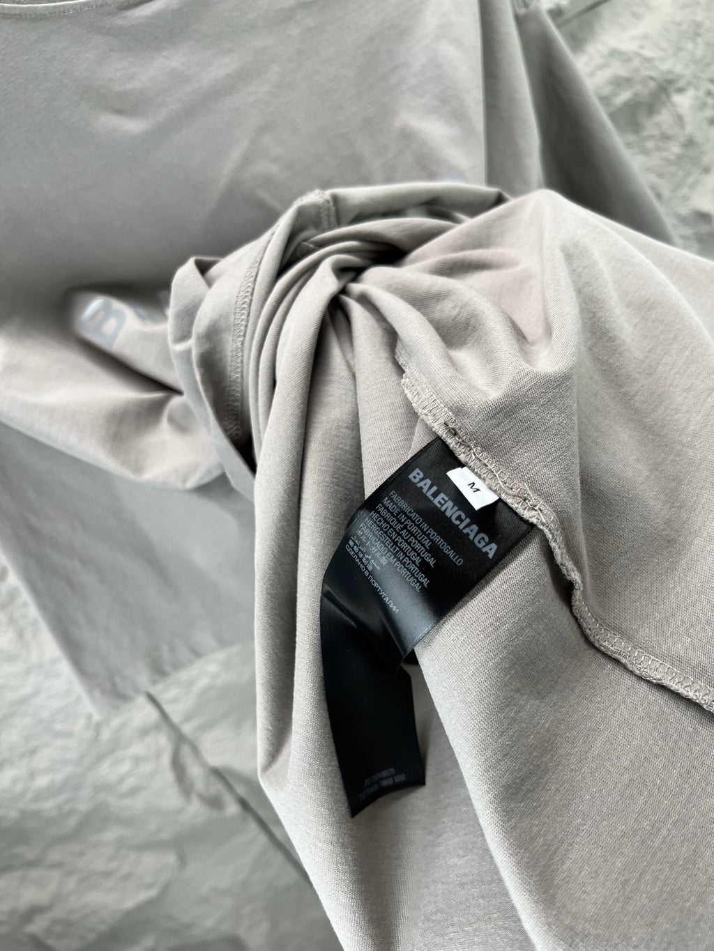 Folded light gray crewneck T-shirt with BALENCIAGA tag and fabric drape