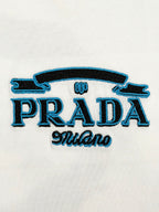 Close-up of embroidered PRADA logo with blue stylized text on white T-shirt