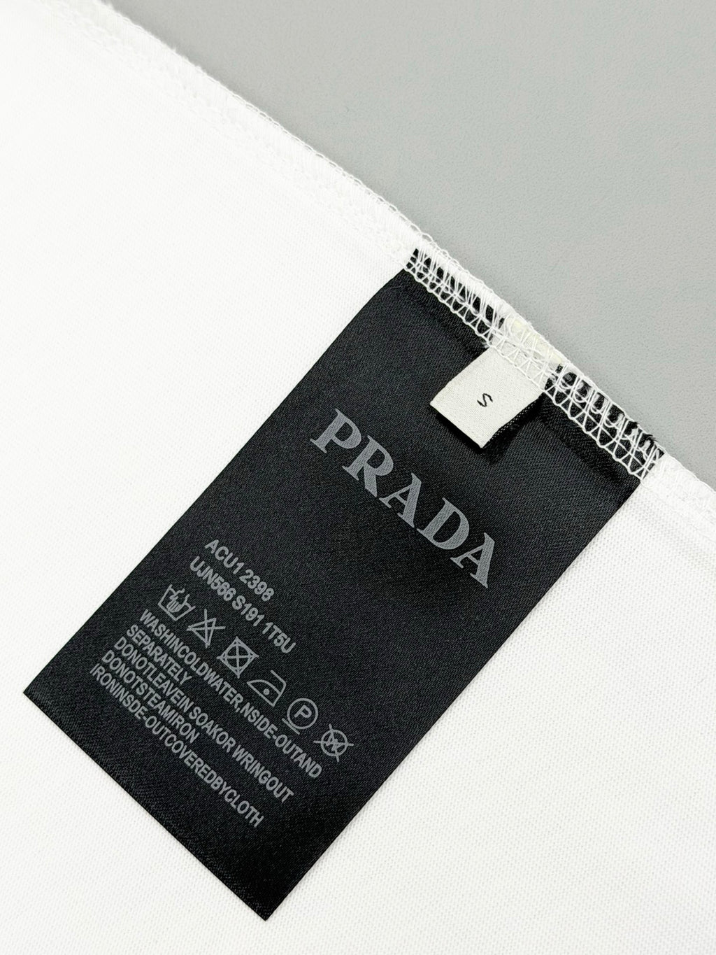Black PRADA size and care label inside white T-shirt hem