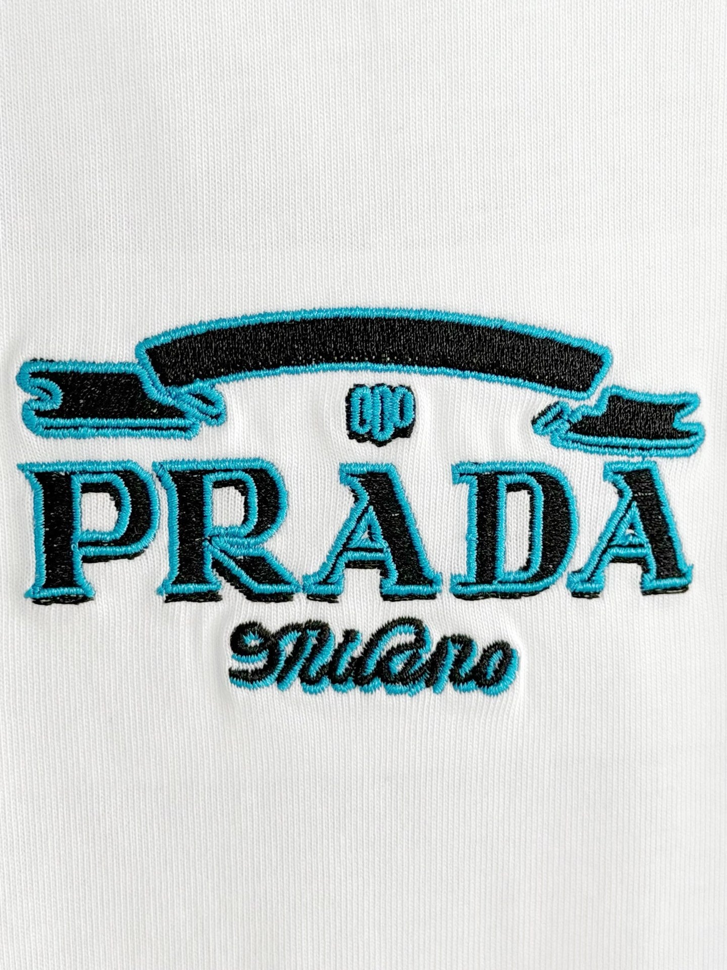 Prada Milano logo embroidery on white T-shirt, blue and black thread