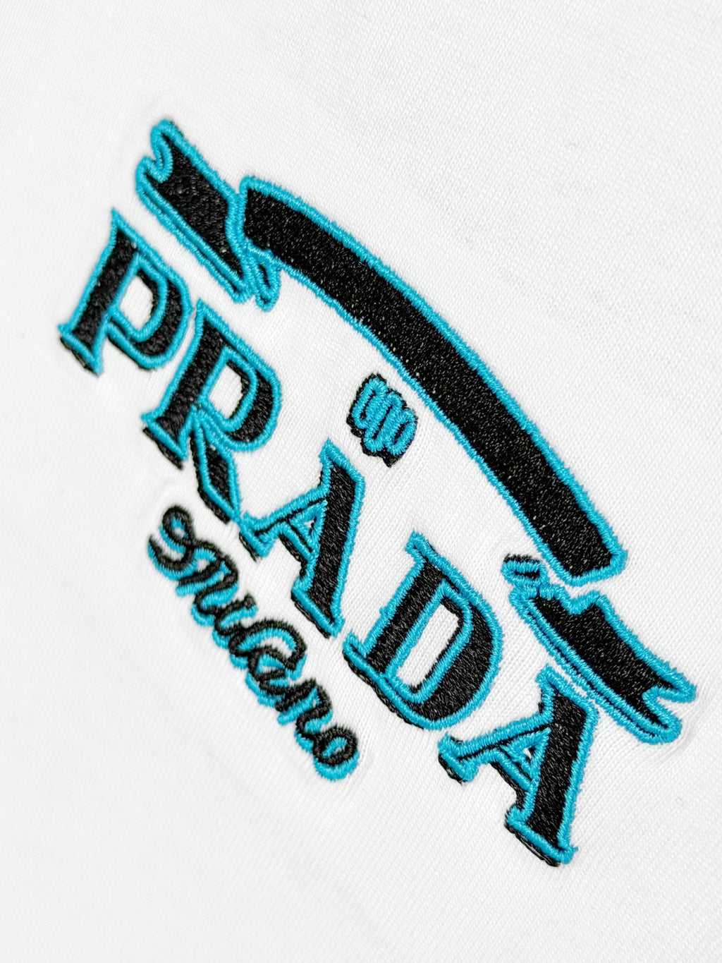 Prada Milano embroidery detail on white T-shirt with blue accents