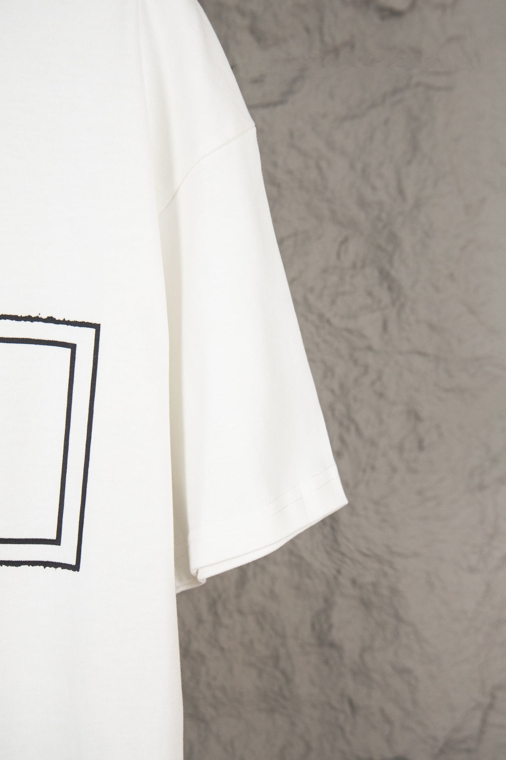 White short-sleeve T-shirt hem and side seam, with partial black graphic on left
