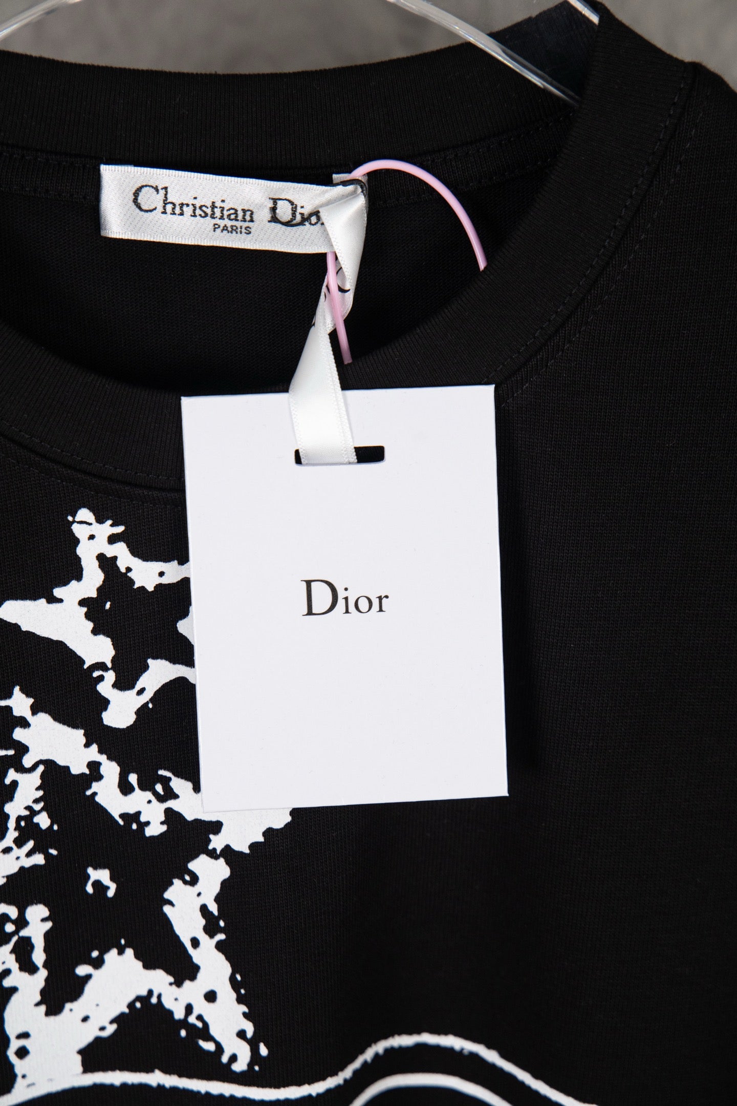 Black T-shirt with white star print and Dior brand hang tag at the collar