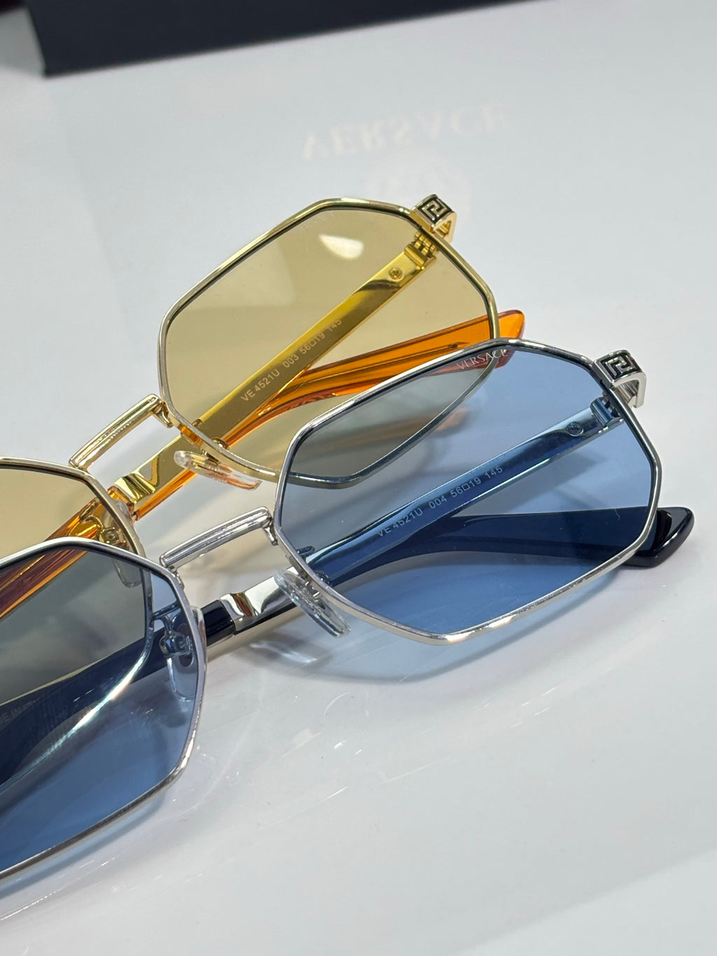 Versace sunglasses close-up: gold frame with yellow lens and blue lens pair.