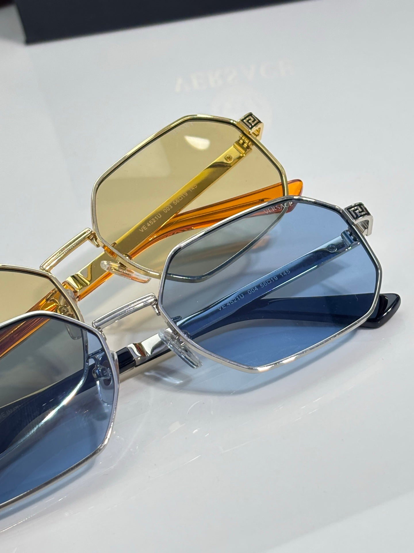 Versace sunglasses close-up: gold frame with yellow lens and blue lens pair.