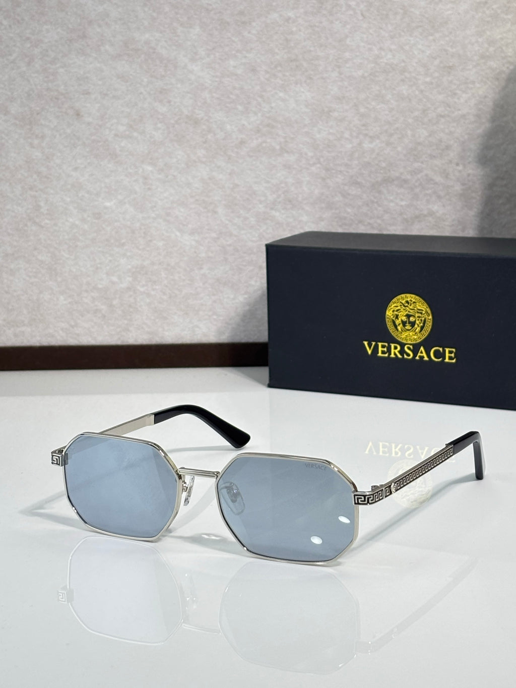 Versace sunglasses with silver frames and light blue hexagonal lenses.
