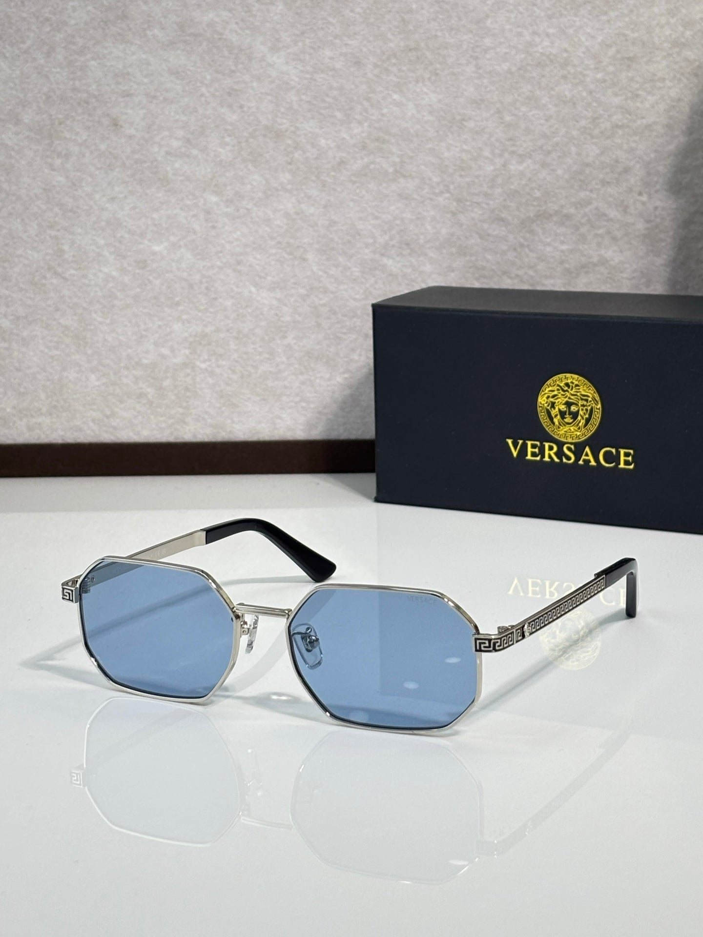 Versace sunglasses with silver frames and light blue tinted octagonal lenses.