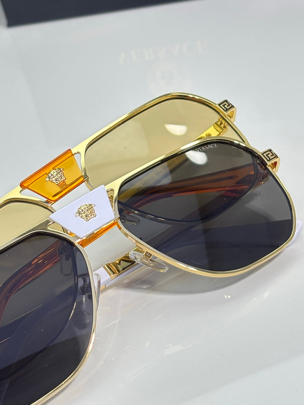 Versace sunglasses close-up: gold frame with orange temple accents and blue-tinted lenses