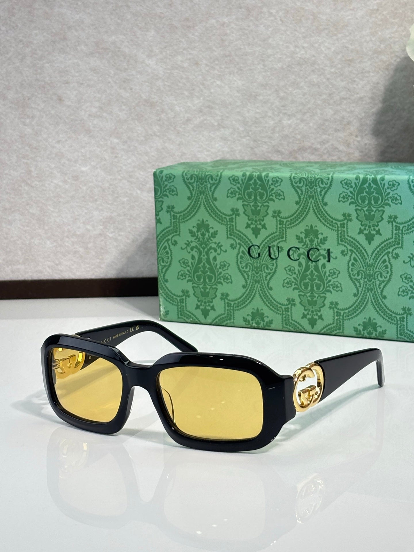 Gucci sunglasses, black frames with gold emblem and yellow-tinted lenses.