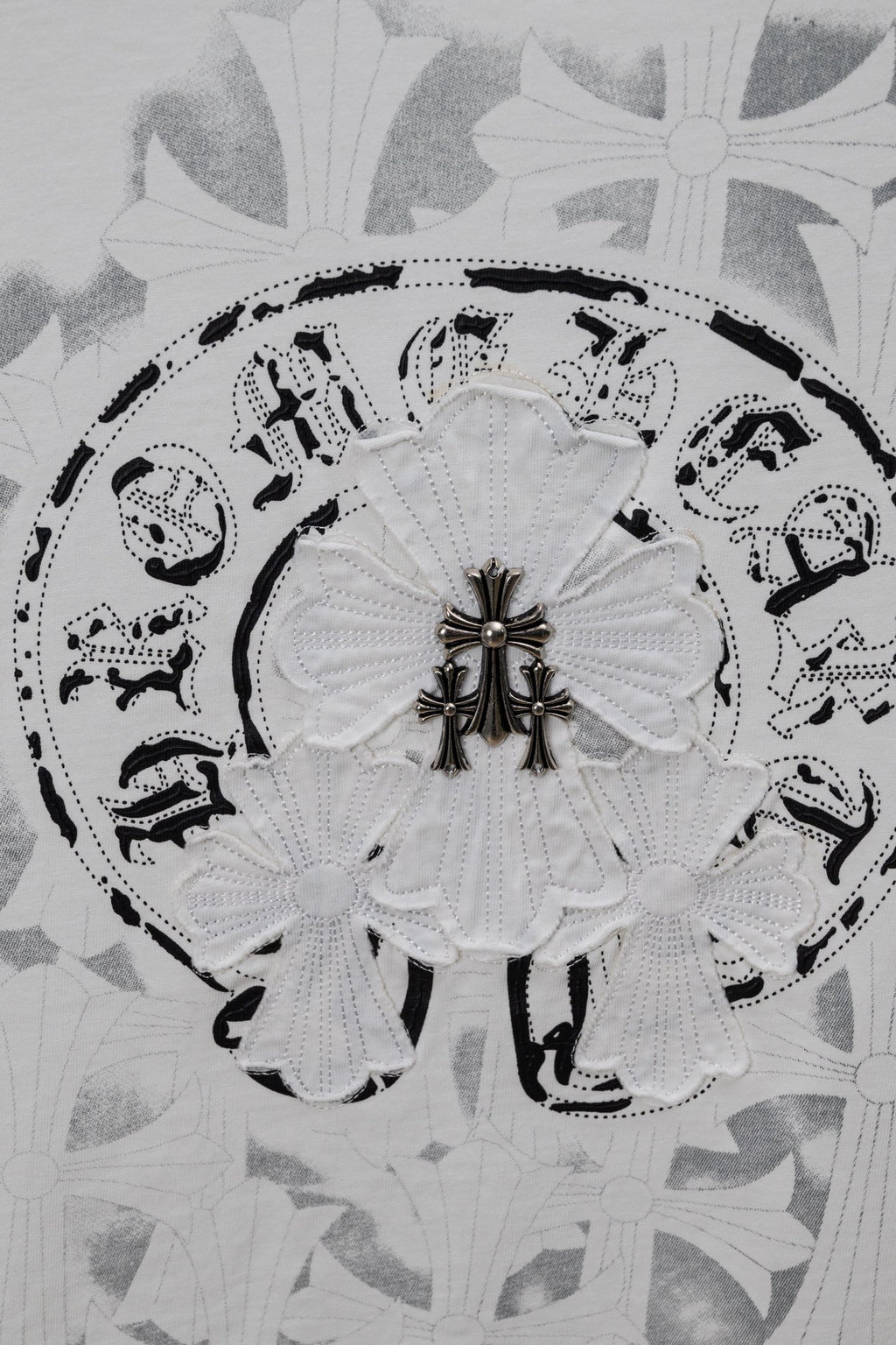 Circular emblem graphic on a light T-shirt fabric with decorative fleur details