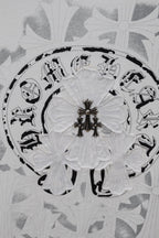 Circular emblem graphic on a light T-shirt fabric with decorative fleur details
