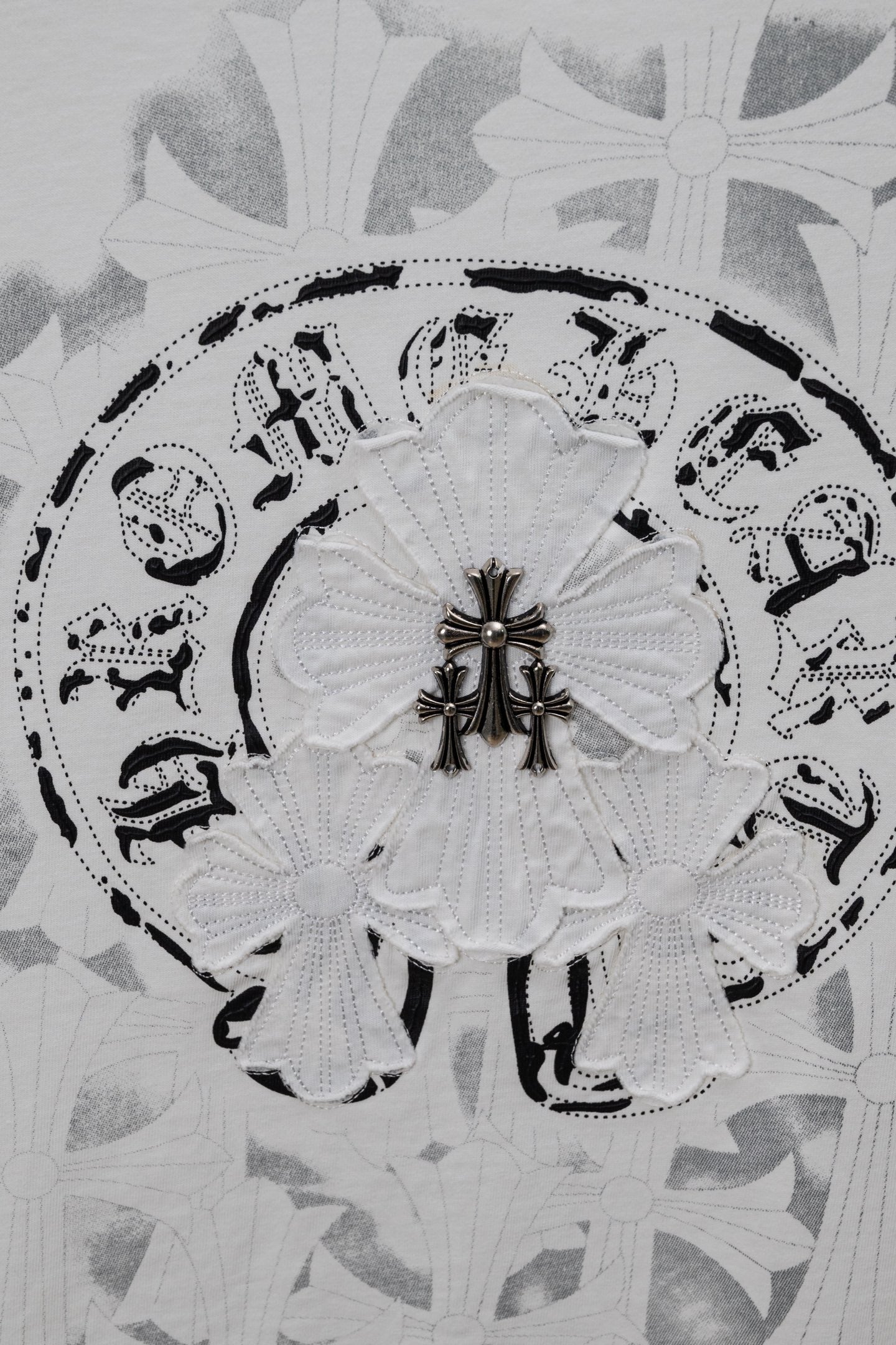 Circular emblem graphic on a light T-shirt fabric with decorative fleur details