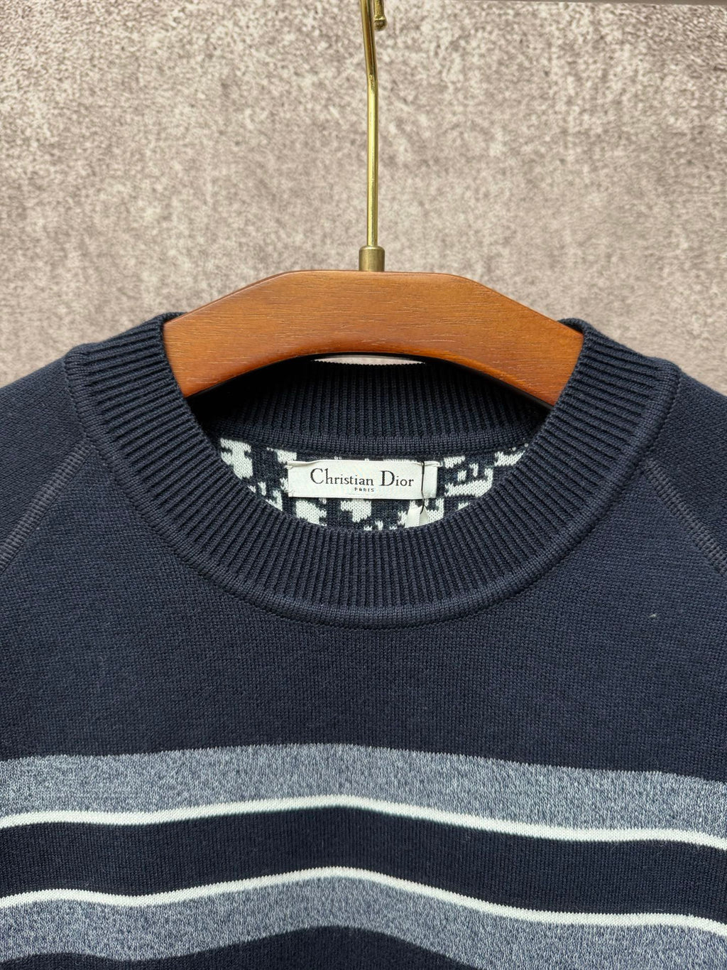 Navy crewneck sweater with light gray and white horizontal stripes near the collar