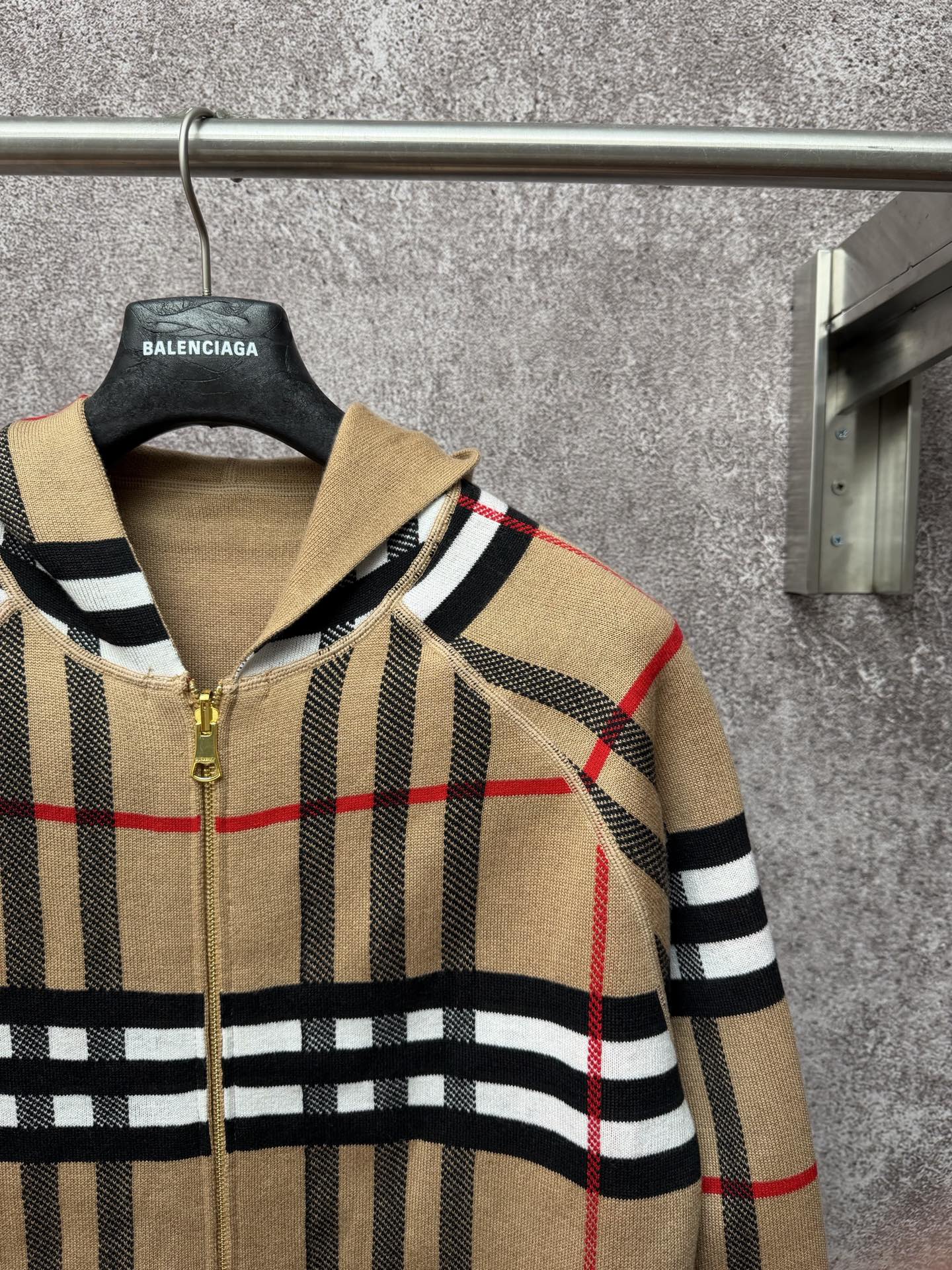 Beige plaid zip-up hoodie on hanger, gold zipper, black and red stripe pattern