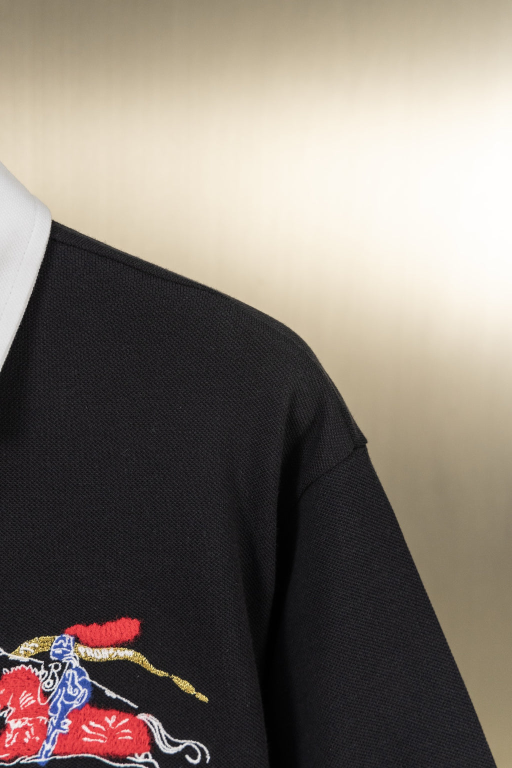 Side view of black polo shirt with embroidered knight-and-horse logo