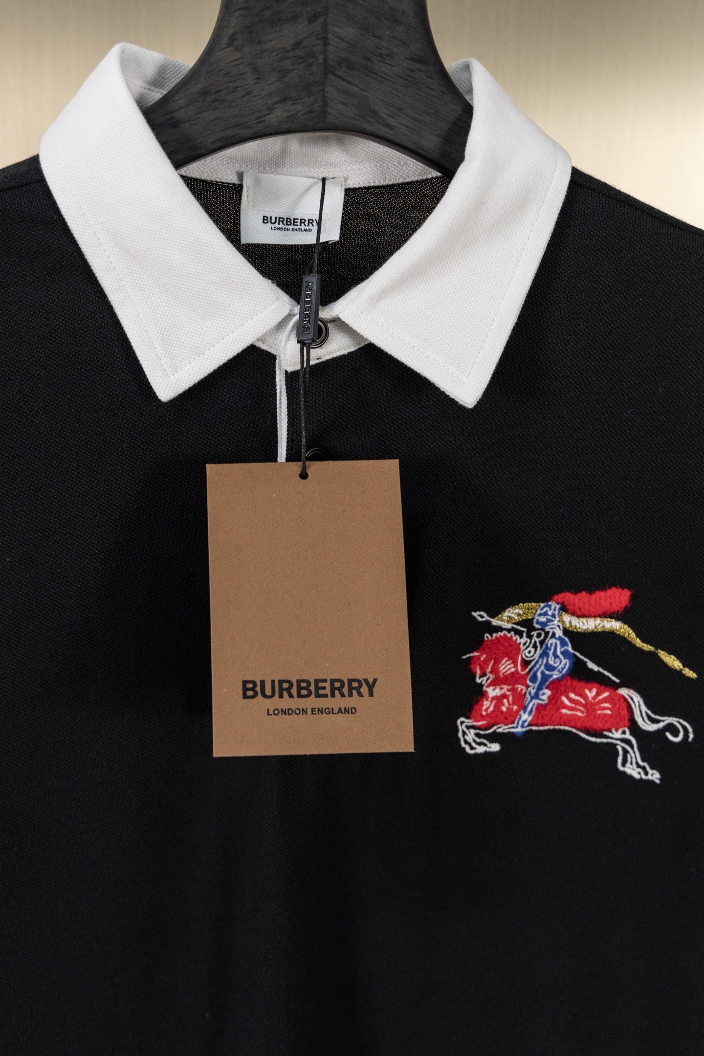Black polo shirt with white collar, embroidered knight-and-horse logo, and hanging tag