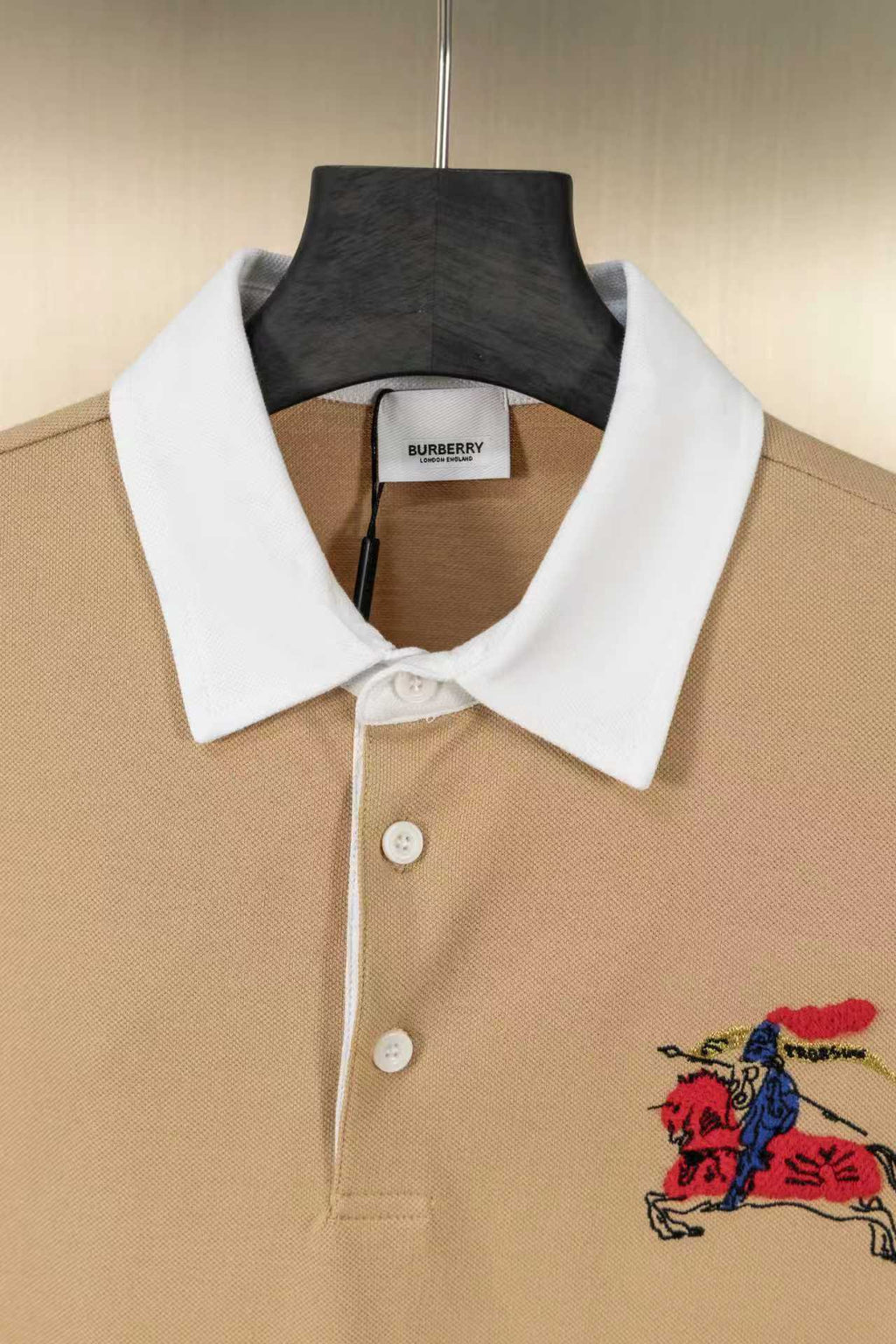 Tan polo shirt with white collar, button placket, and colorful horse emblem