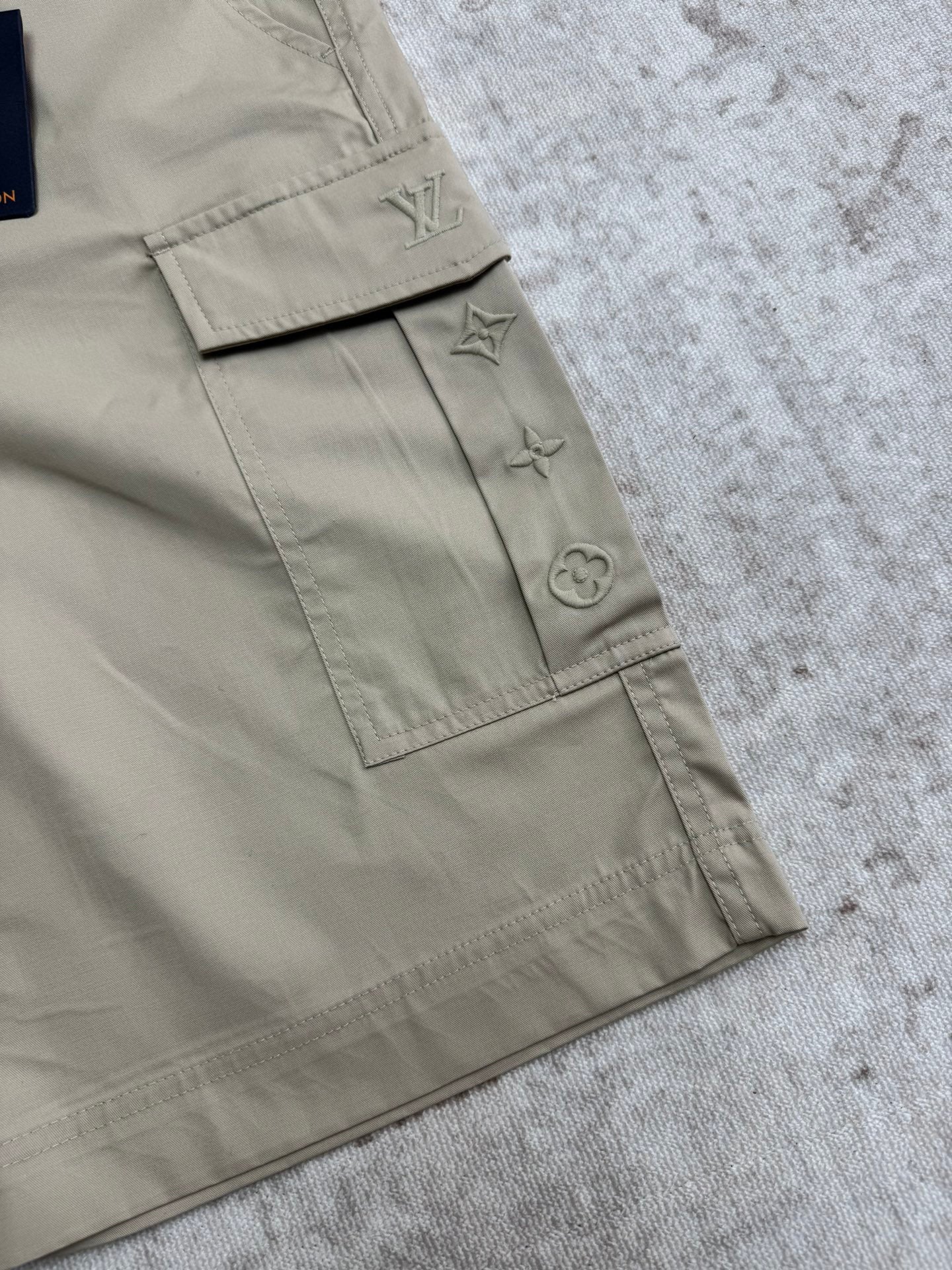 Beige cargo shorts detail with stitched logo patch and inner tag