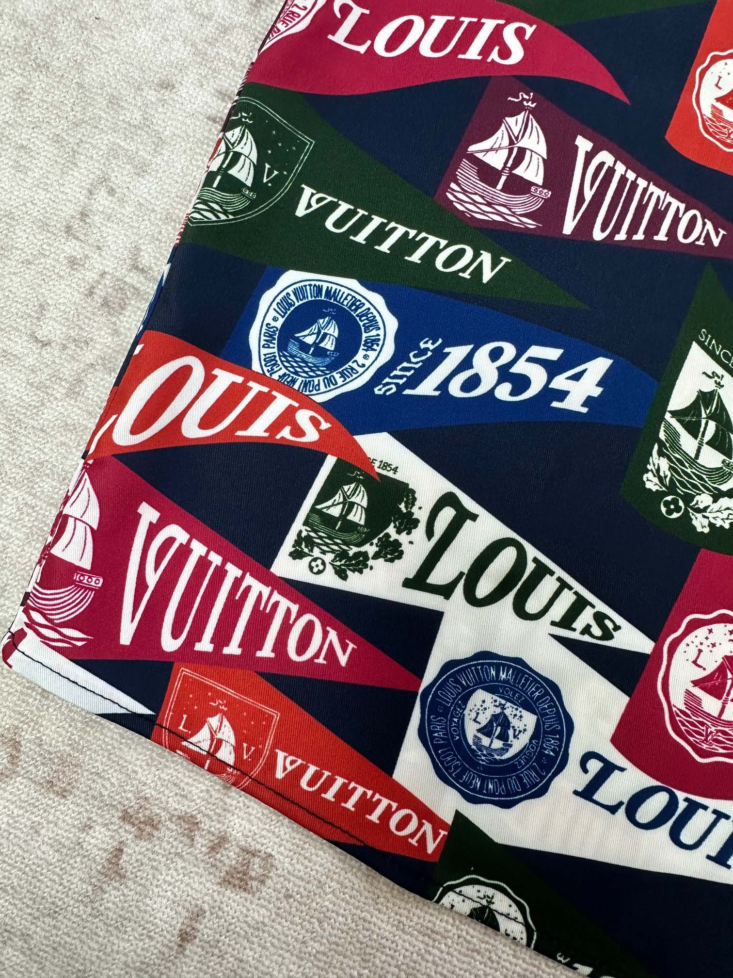 Short-sleeve shirt fabric close-up with multicolor Louis Vuitton crest and logo print