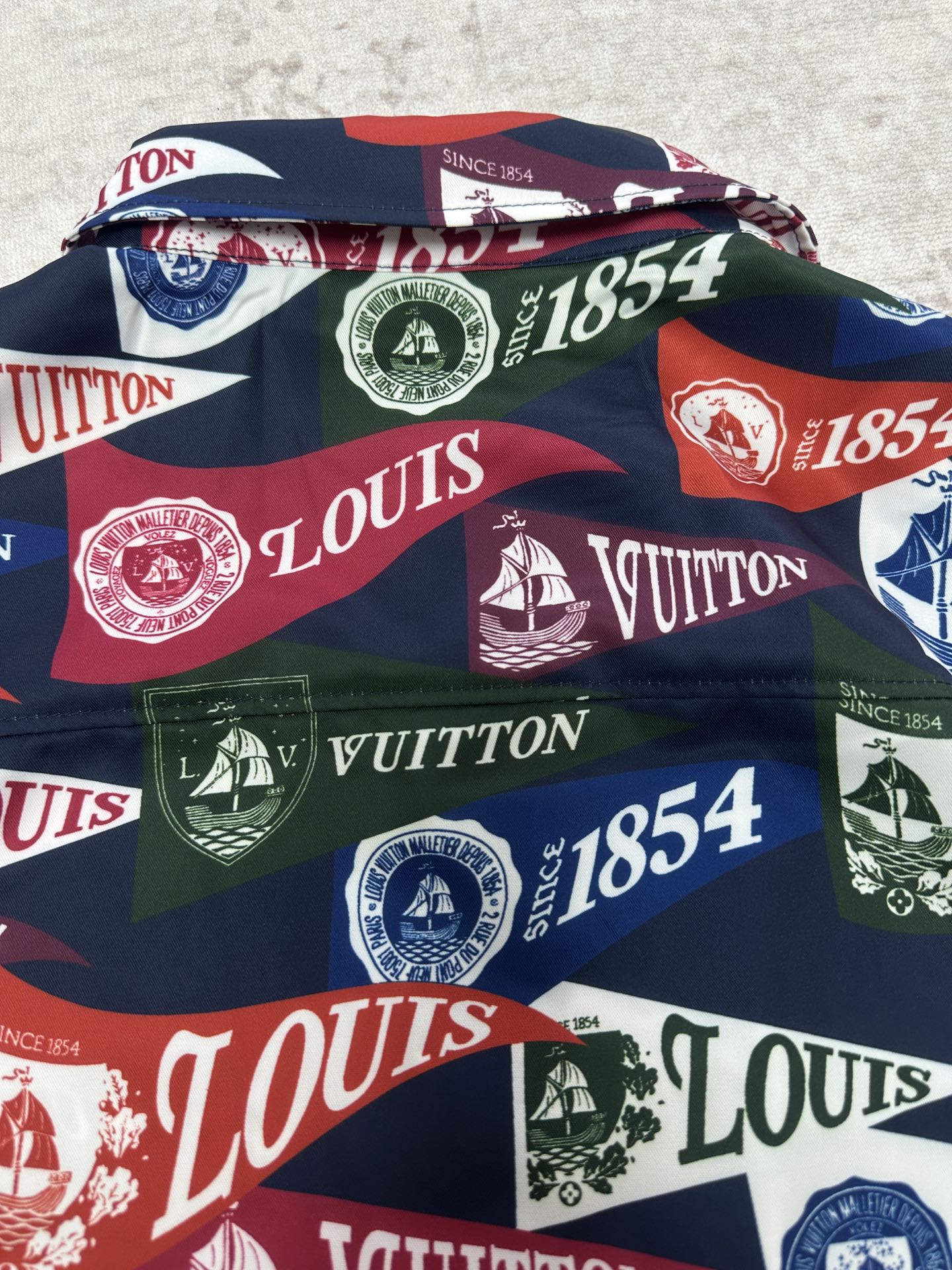 Short-sleeve shirt laid flat showing bold multicolor Louis Vuitton crest and logo pattern