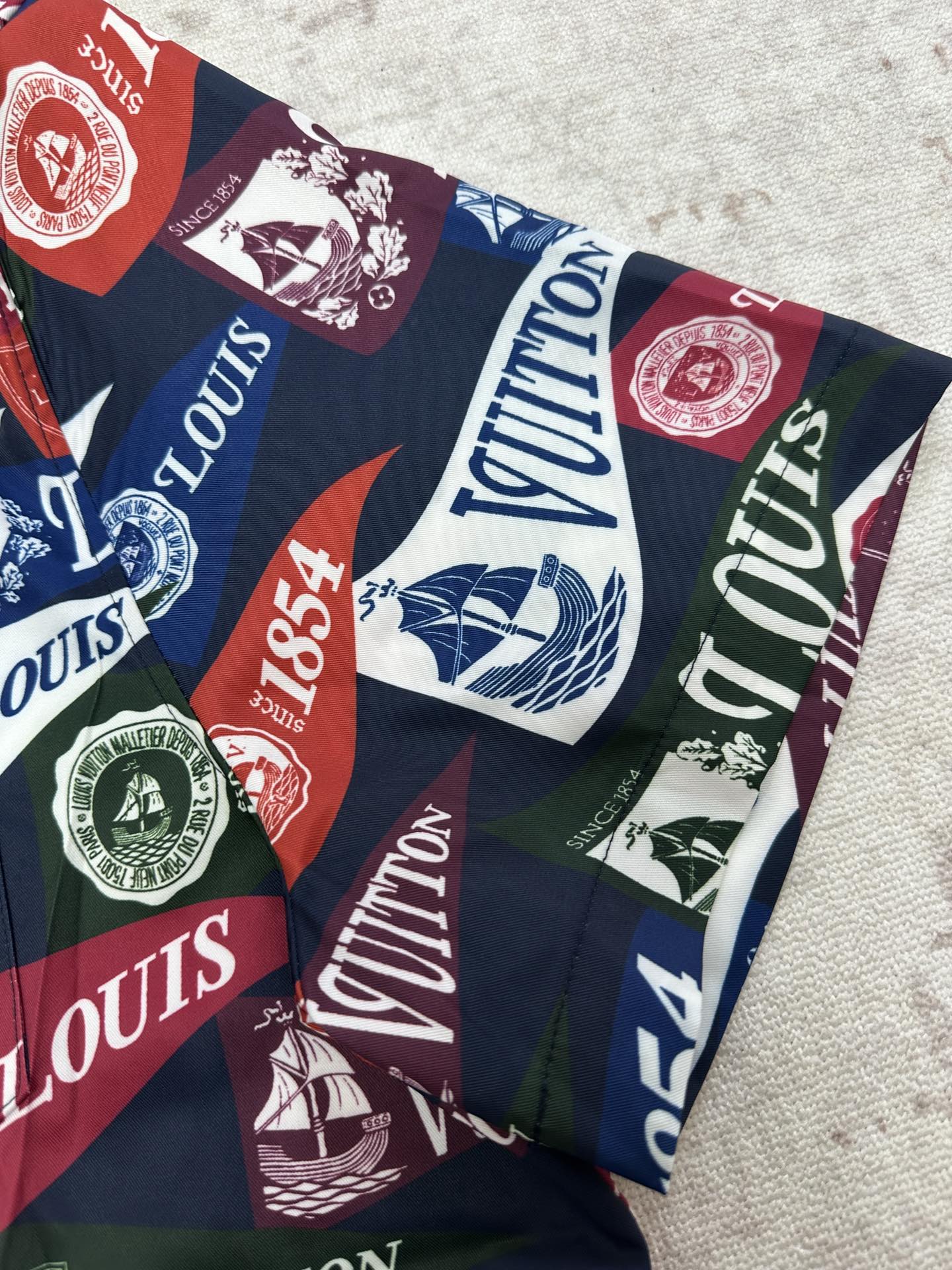 Short-sleeve shirt fabric close-up with multicolor Louis Vuitton crests and logo blocks