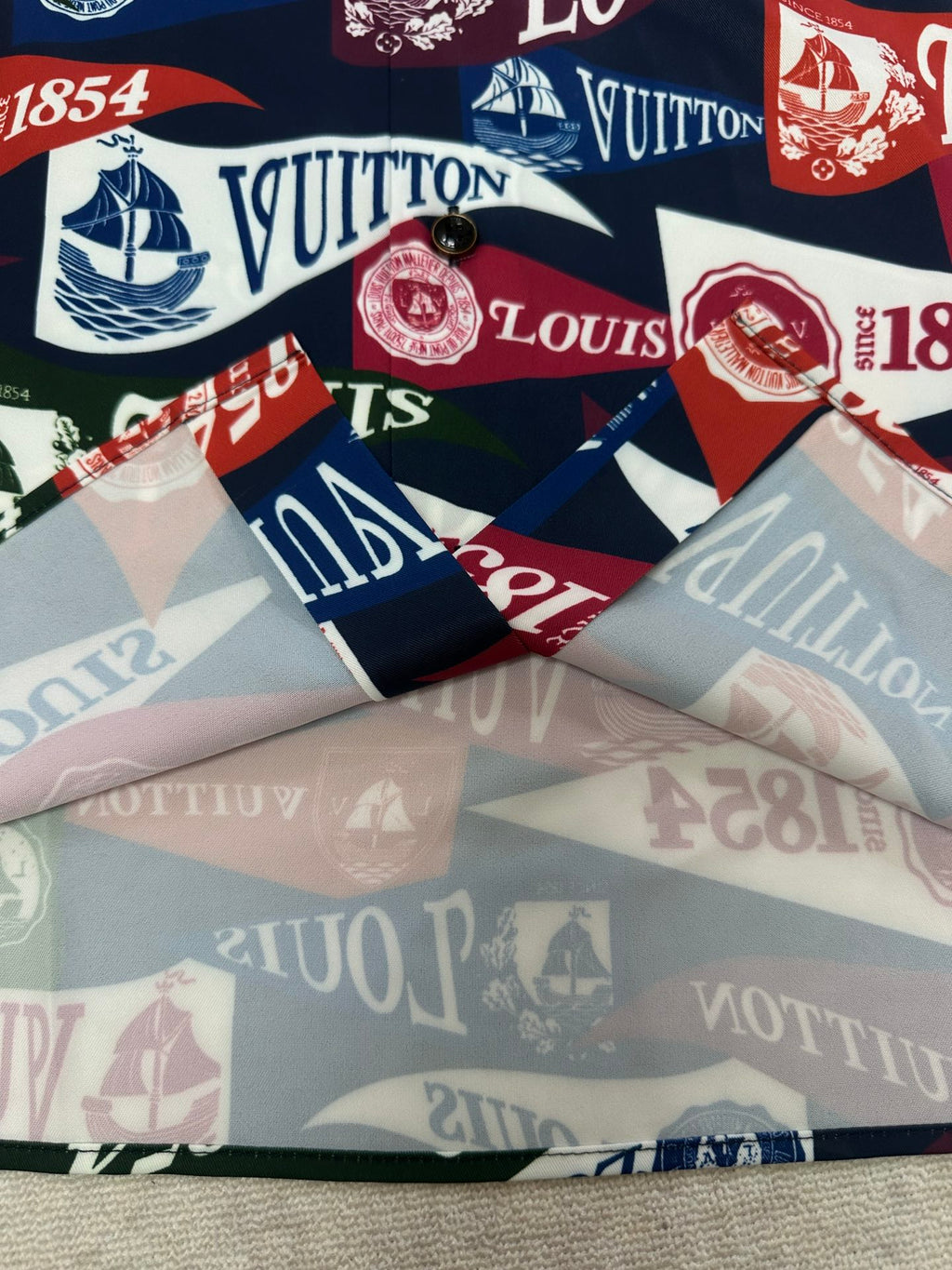 Short-sleeve shirt laid flat showing multicolor Louis Vuitton crest and logo banding